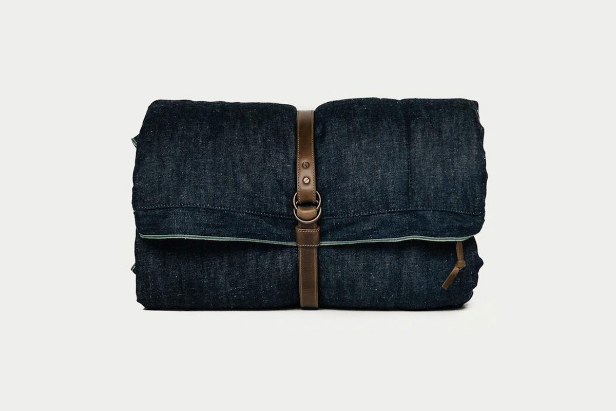 A dark blue, rolled-up blanket secured with a brown leather strap and buckle, placed against a plain light background.