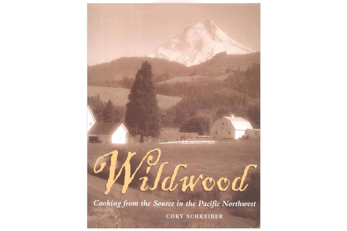 Cover of the book Wildwood: Cooking from the Source in the Pacific Northwest by Cory Schreiber, featuring a sepia-toned rural landscape with barns, trees, and a snow-capped mountain in the background.