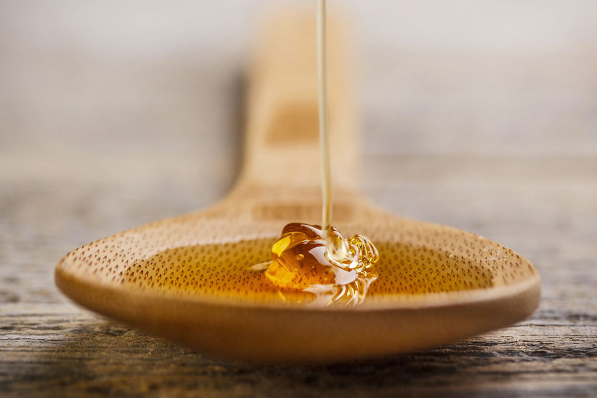Close-up of honey being poured onto a wooden spoon, with a blurred wooden surface in the background.