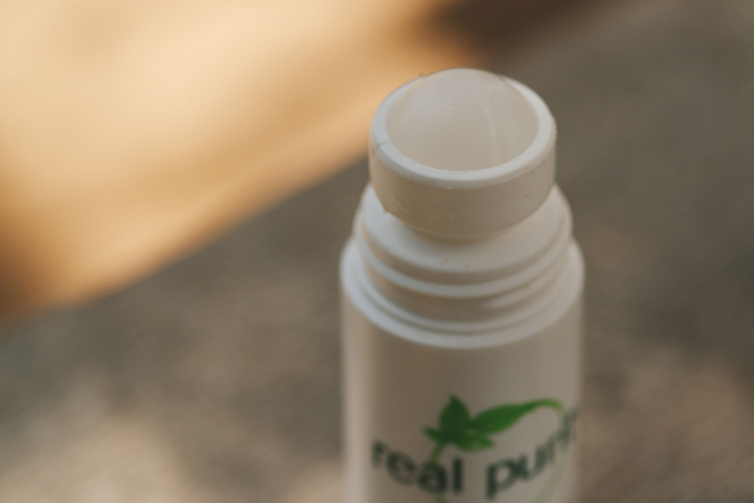 Close-up of the open top of a white lip balm or deodorant tube, showing the smooth, rounded tip and part of a green logo with leaves on the container.