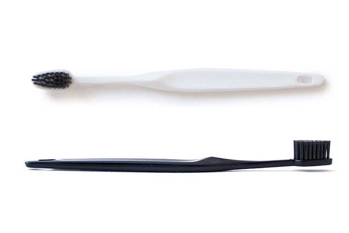 A white toothbrush with black bristles and a black toothbrush with black bristles are placed parallel on a white background.