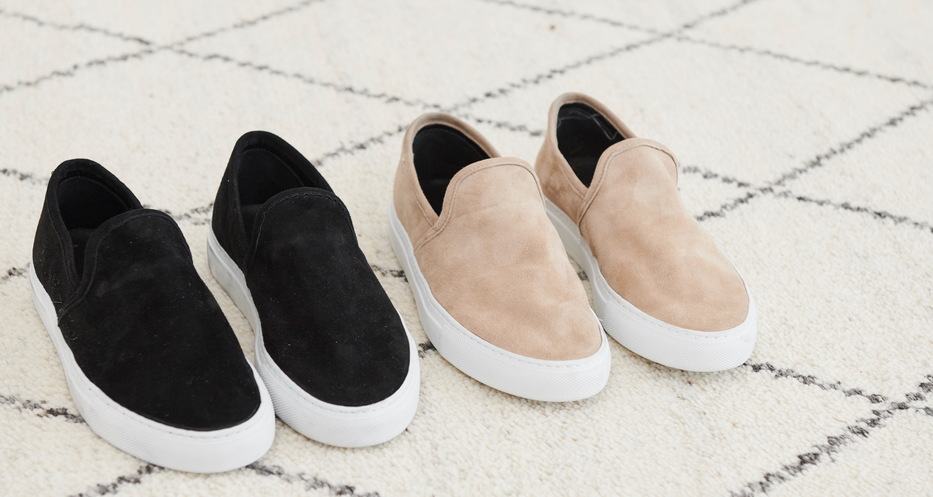 Two pairs of Jenni Kayne Sneakers, one black and one beige with white soles, are placed side by side on a white rug featuring a black grid pattern.