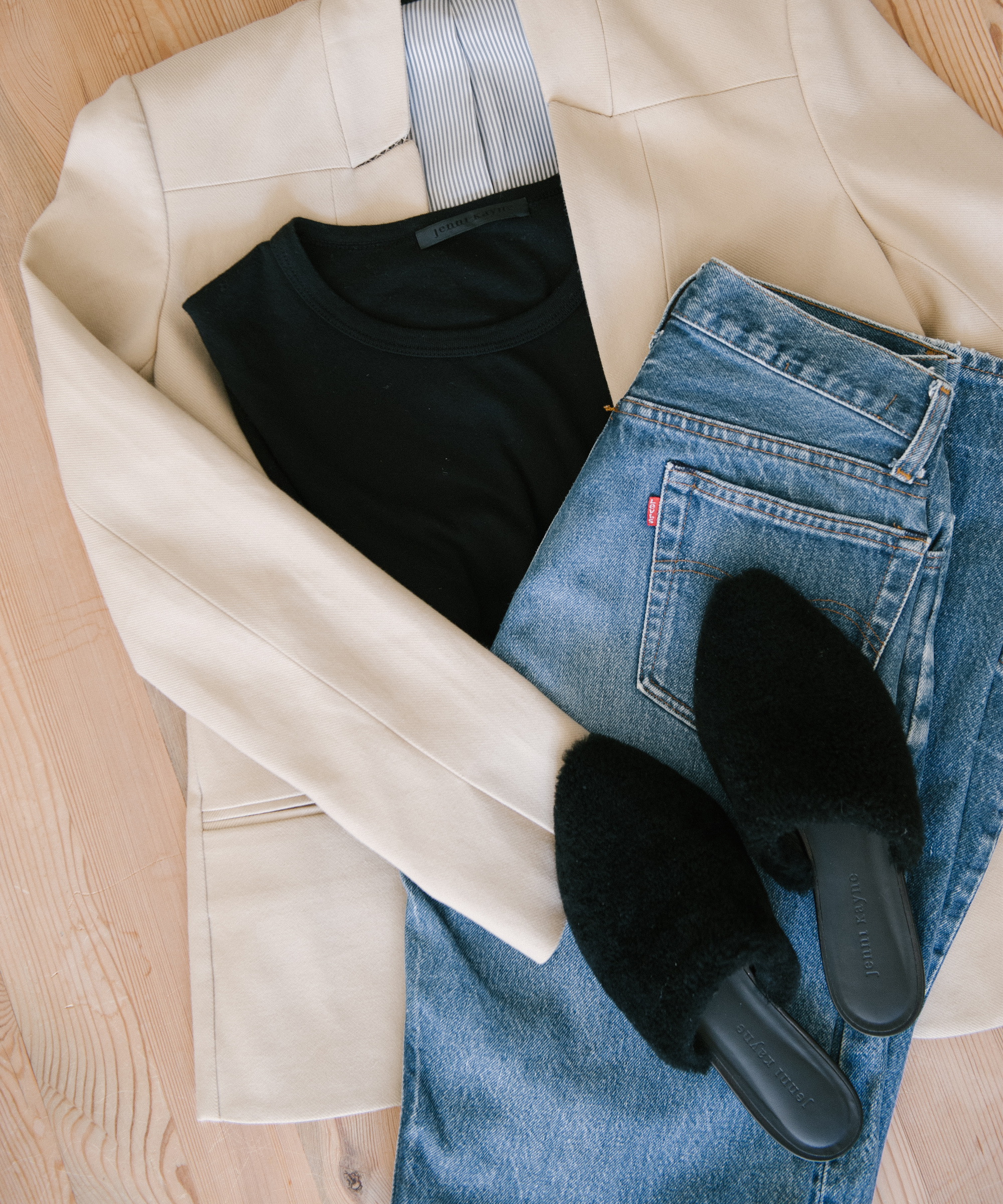 A beige blazer, black top, blue jeans, and black slip-on shoes are neatly arranged on a light wooden surface—perfect inspiration for stylish blazer outfits.