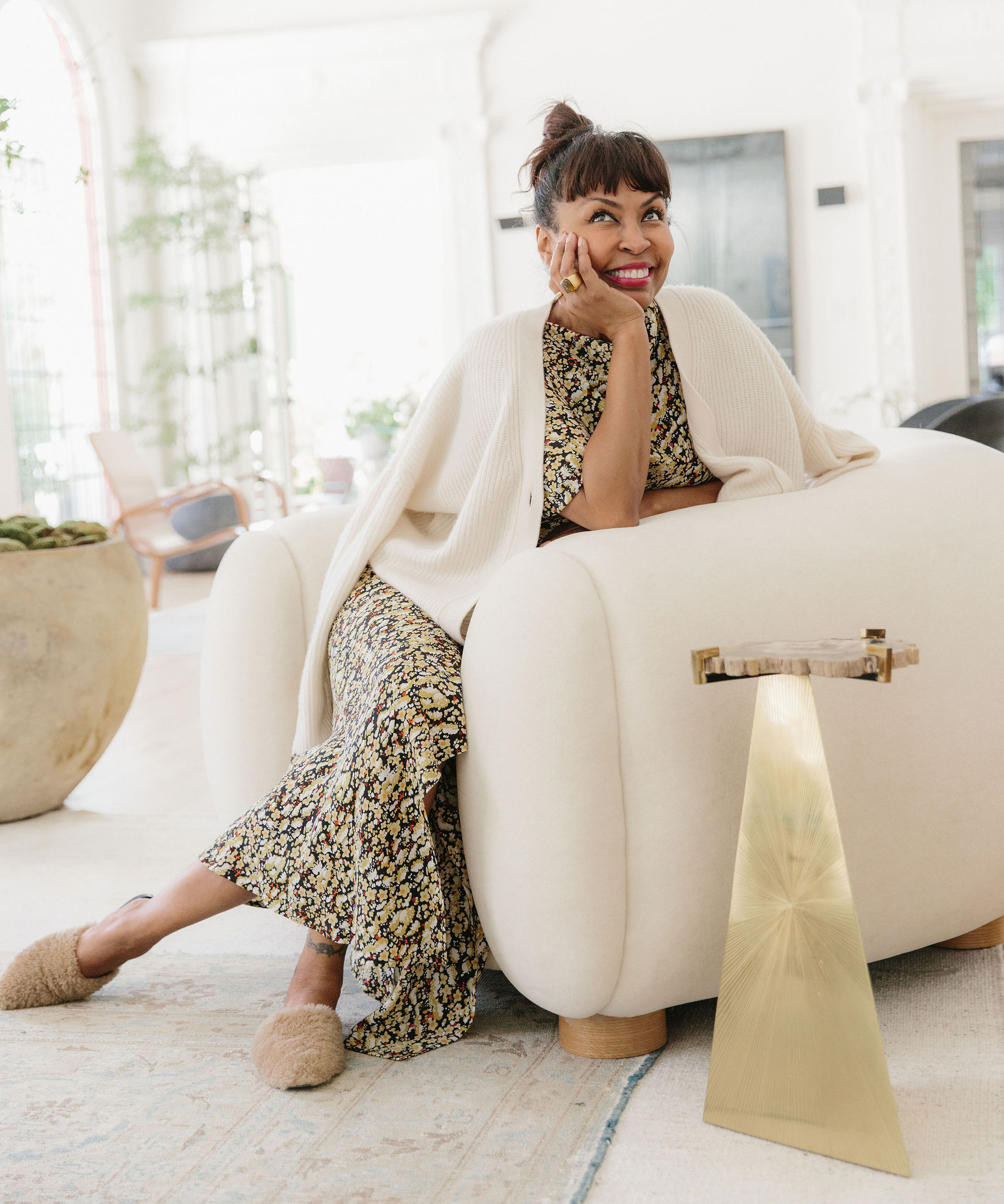 Brigette Romanek posing in large boucle chair with gold side table