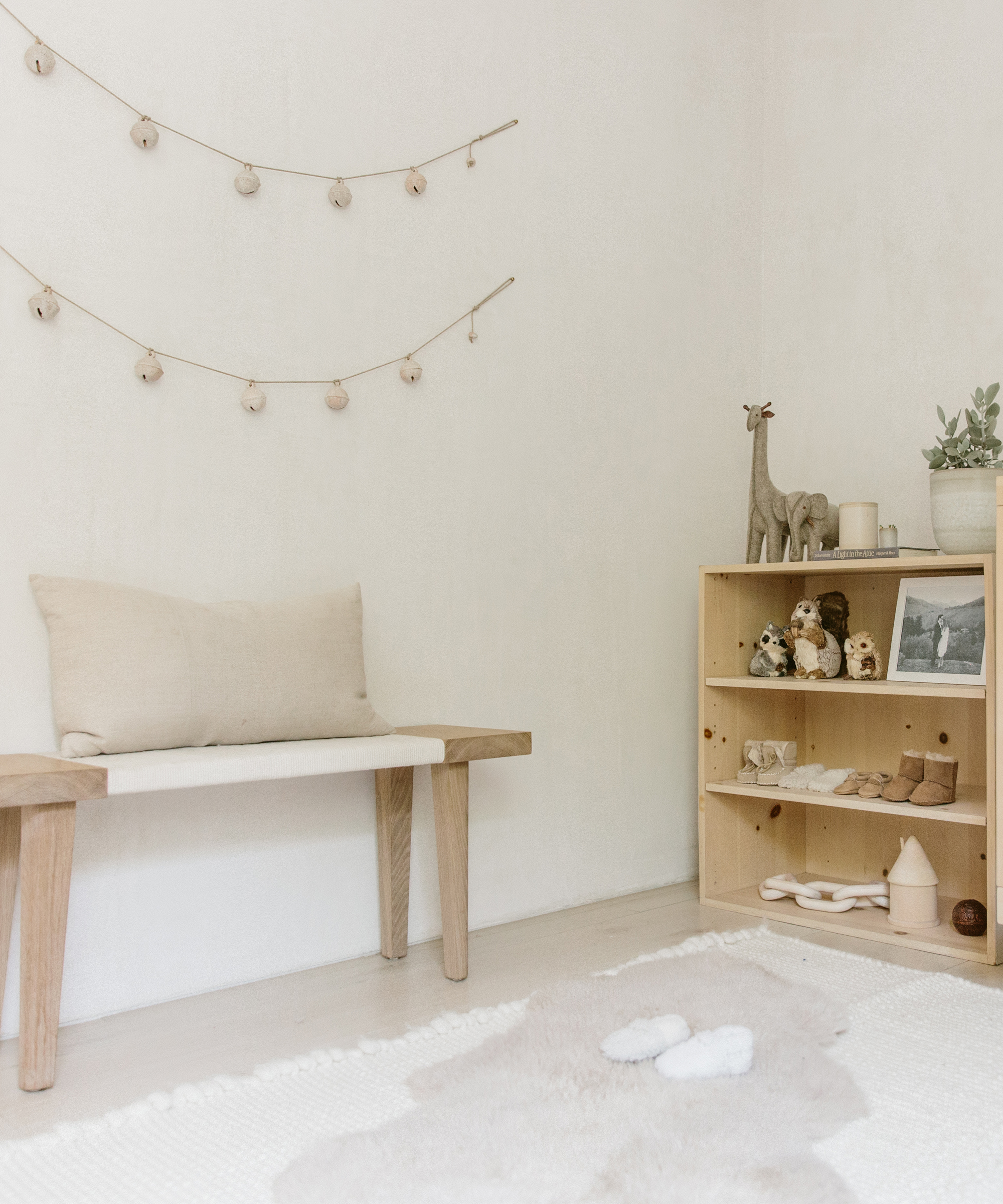 Baby room with wooden bench, cream colored pillow, wooden cabinet, and white walls.
