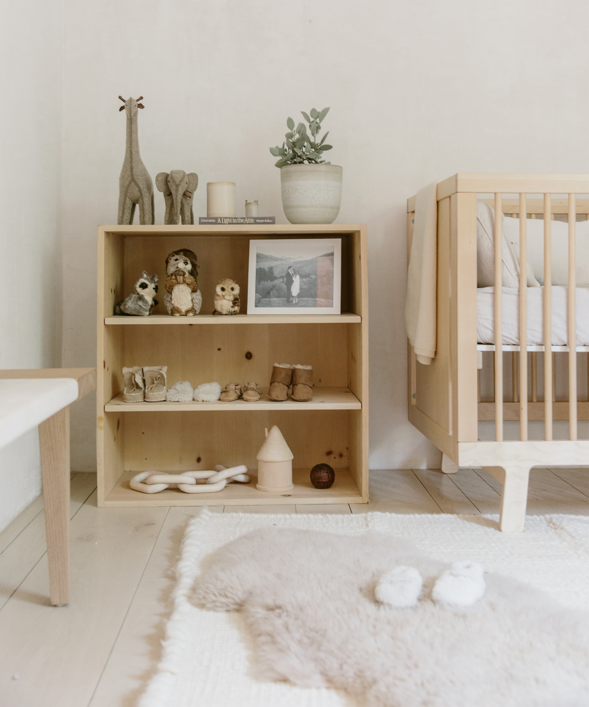 Wooden baby crib, wooden cabinet, white rug, and white walls.