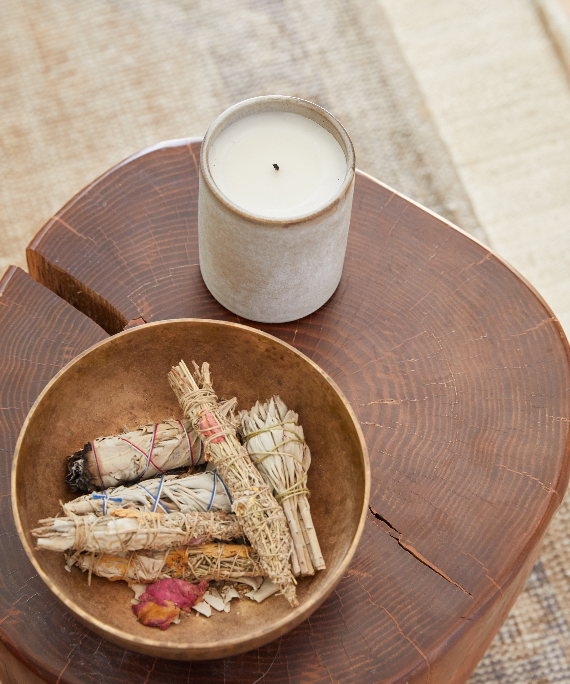 A white candle with dried, wrapped herbs in a bowl on a wooden small table.