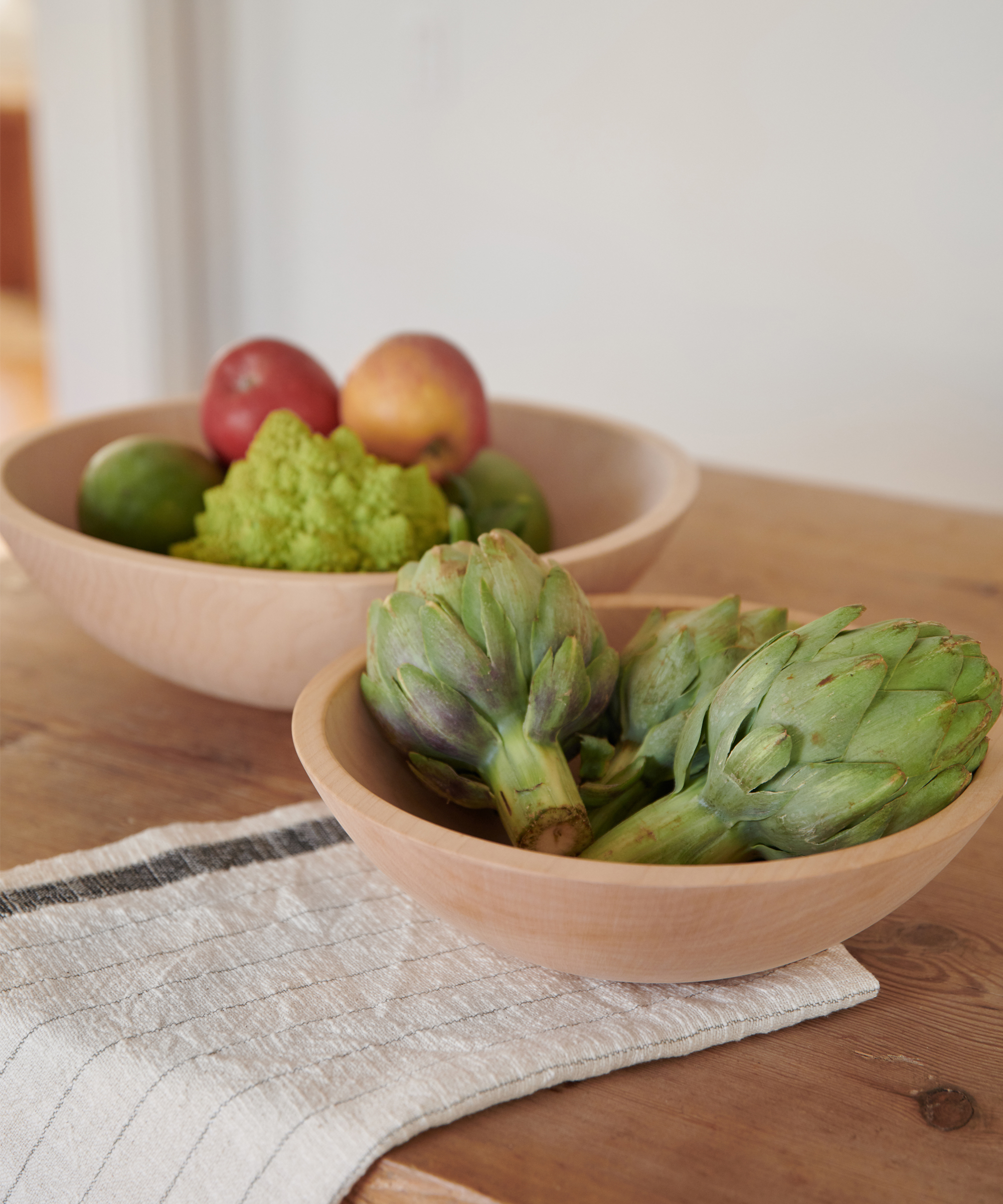 Artichoke and fruits in a bowl placed on a wood table.