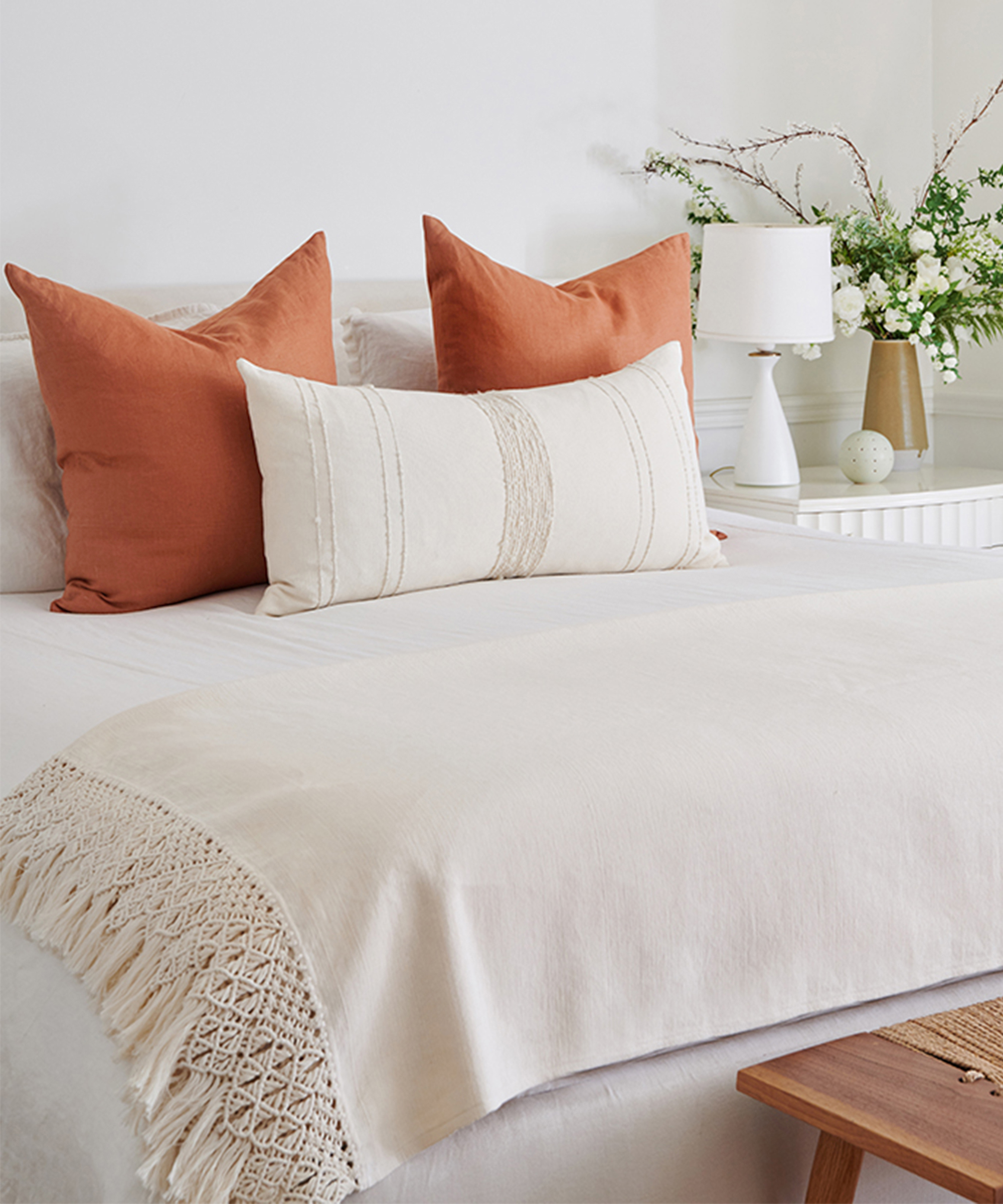 White bed with orange pillow and an ivory colored throw blanket.