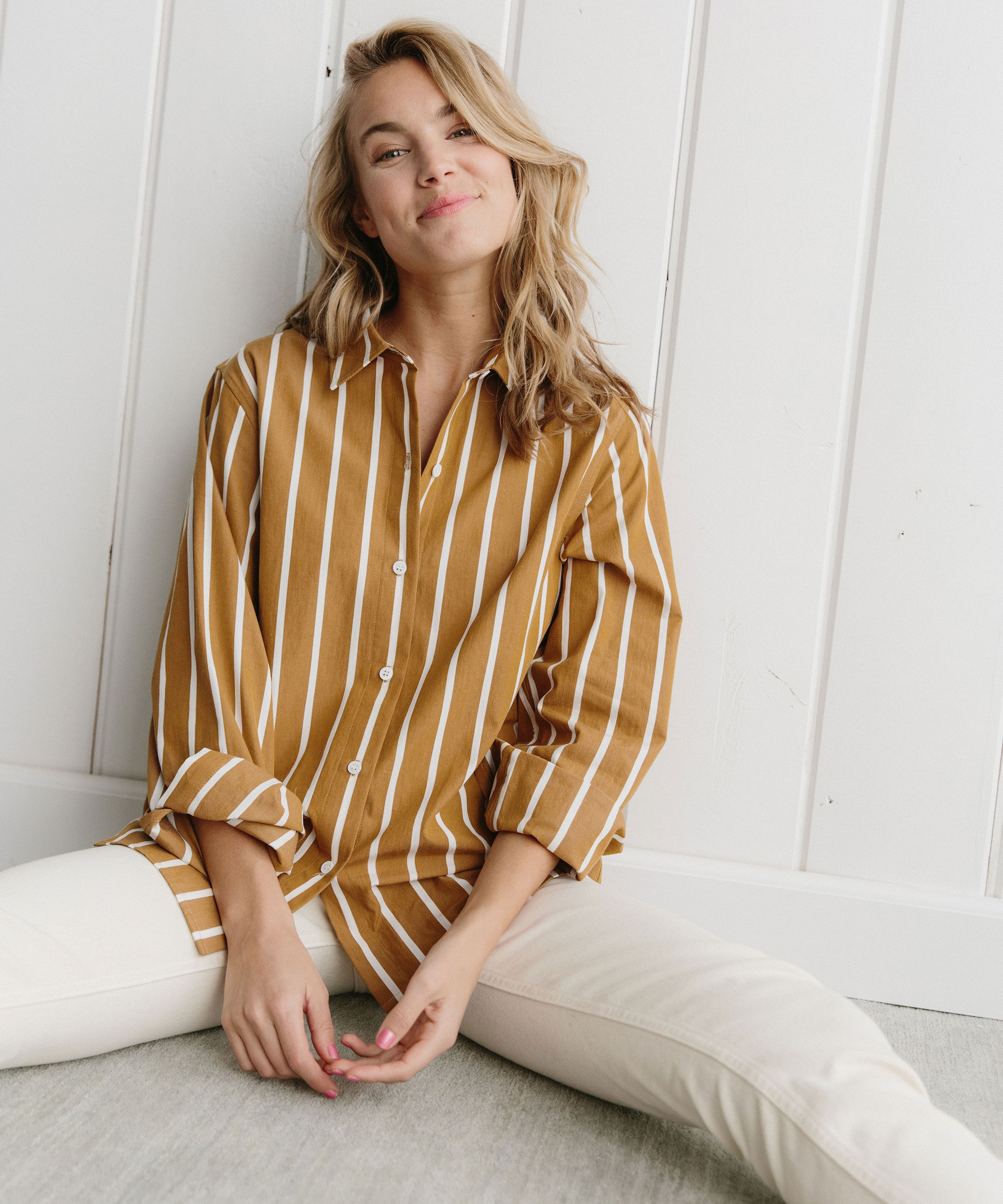 Woman sitting on the ground wearing button up shirt and white jeans.