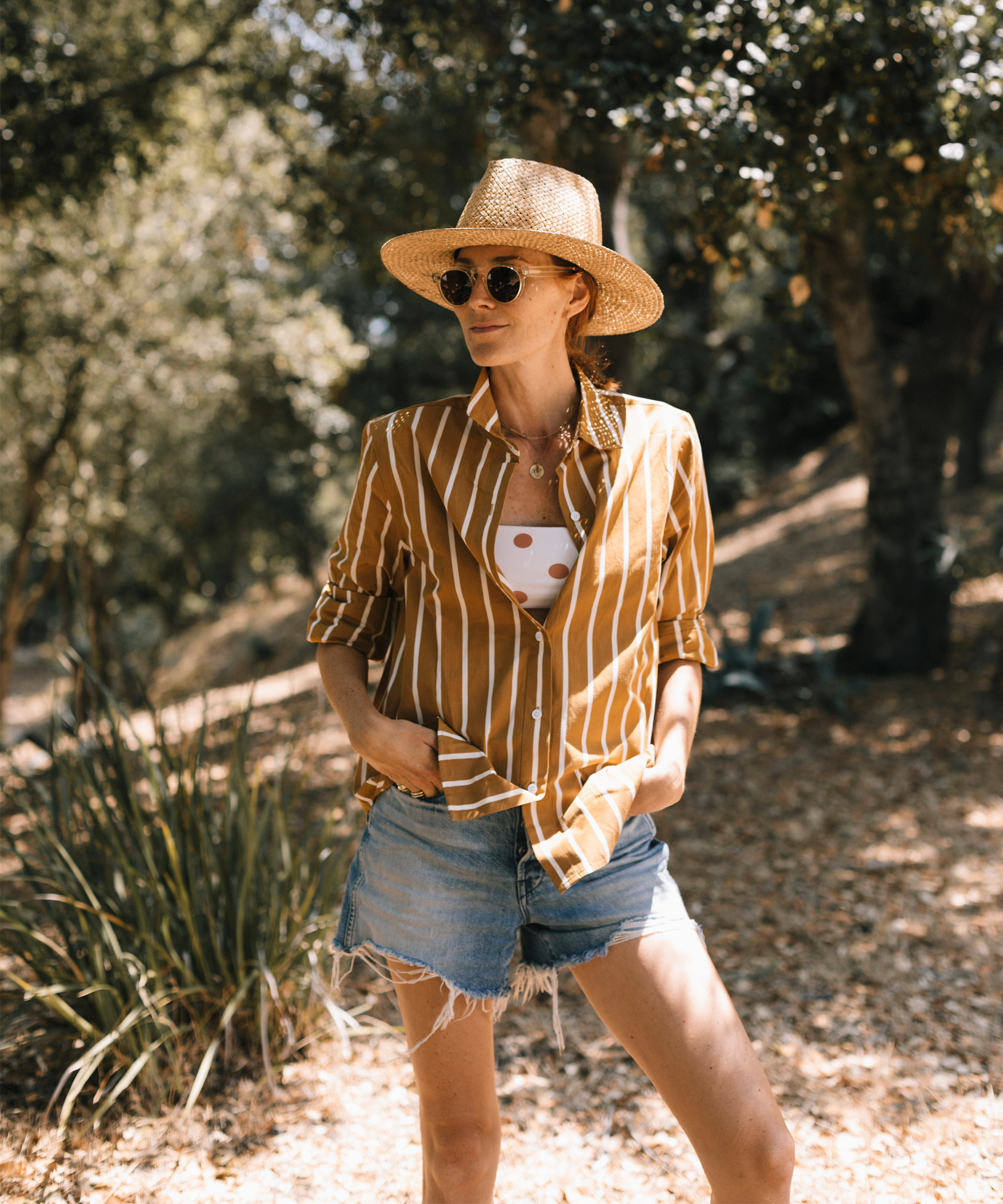 Woman wearing sun hat, white and brown button up shirt, and sunglasses.