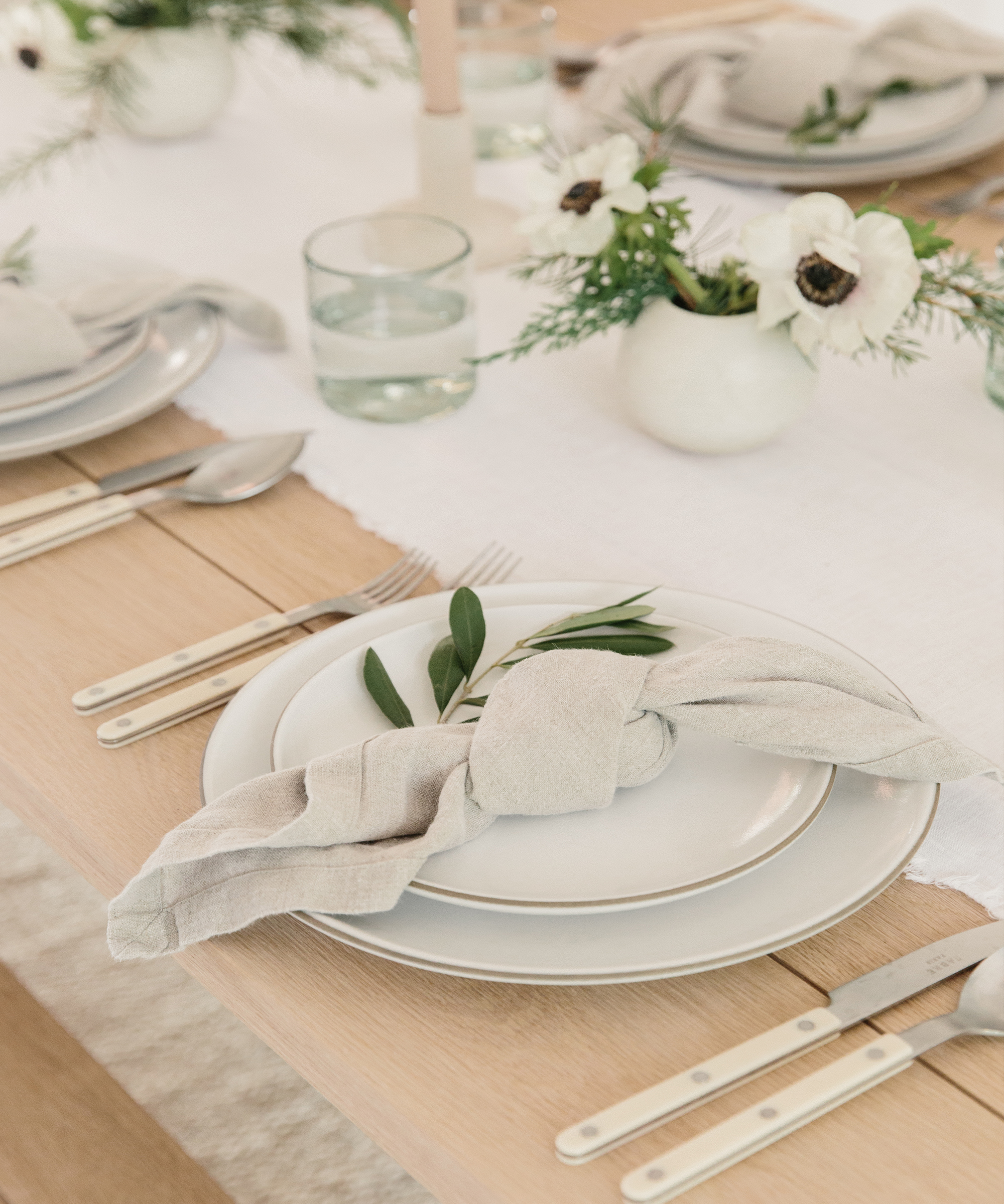 Jenni Kayne oak dining table with ceramic dinnerware, neutral table runner and napkins, and holiday greenery.