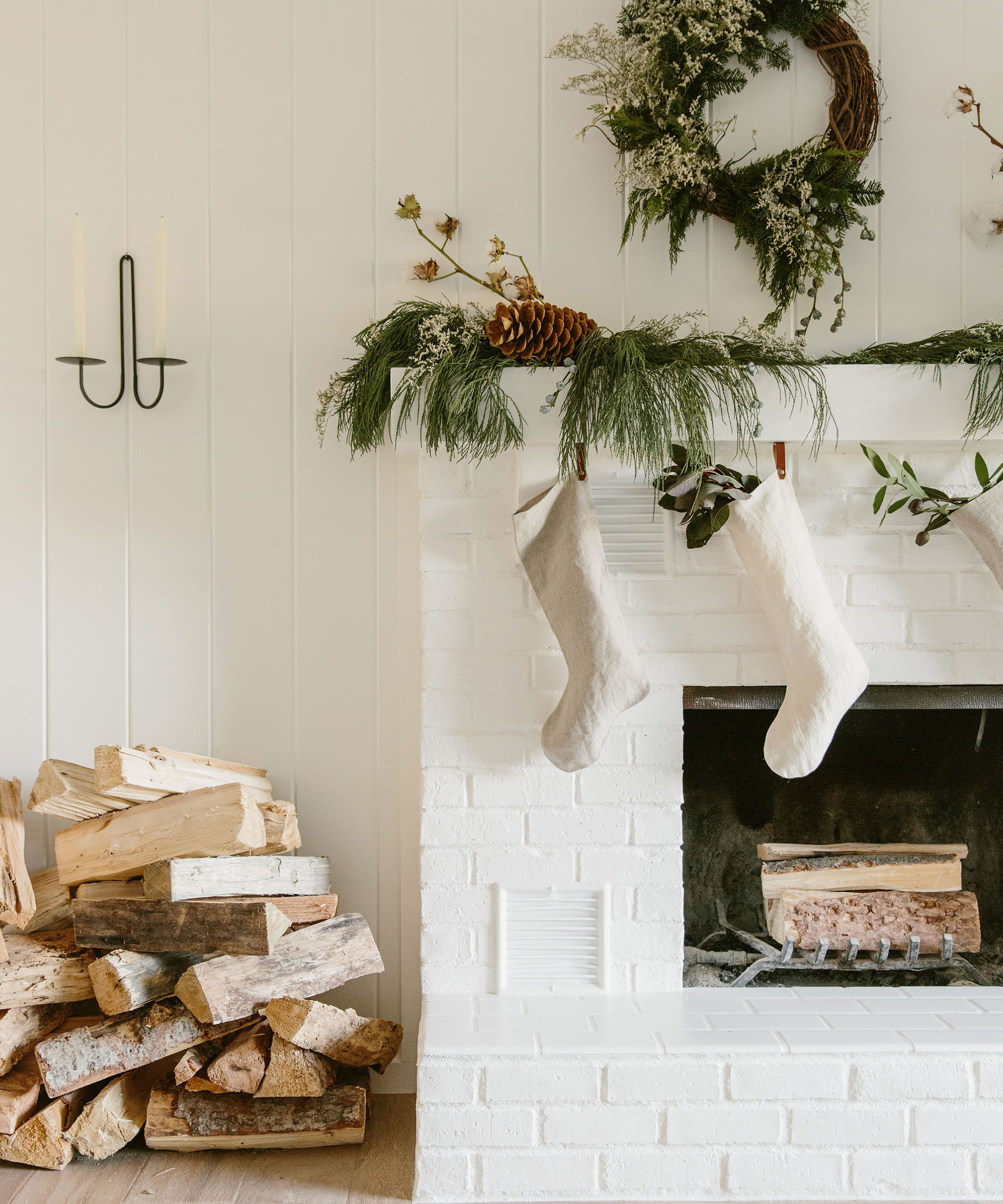 Holiday home with white fireplace, stockings, stack of wood, and holiday greenery above the mantle.