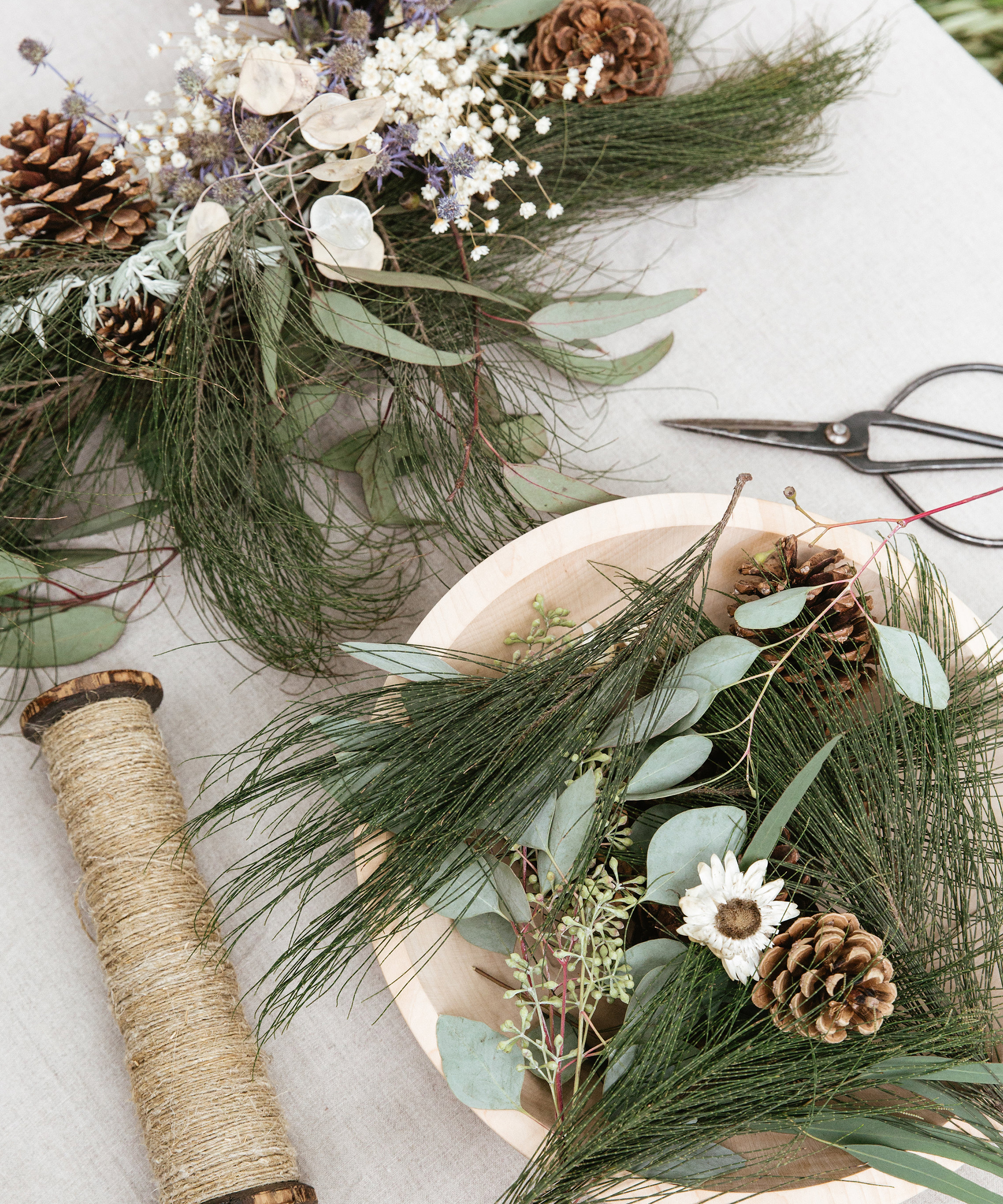 Wreath-making essentials like pinecones and fir on top of a table.