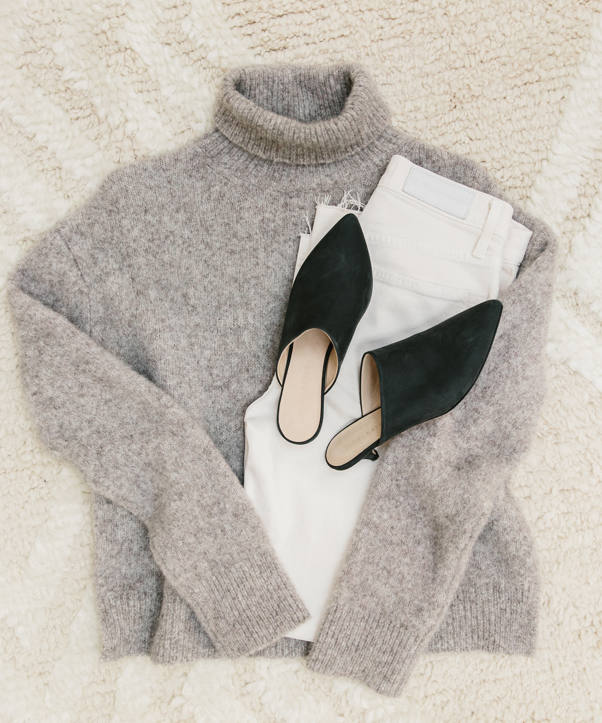 Turtleneck sweater and black kitten heel laydown on a patterned rug.
