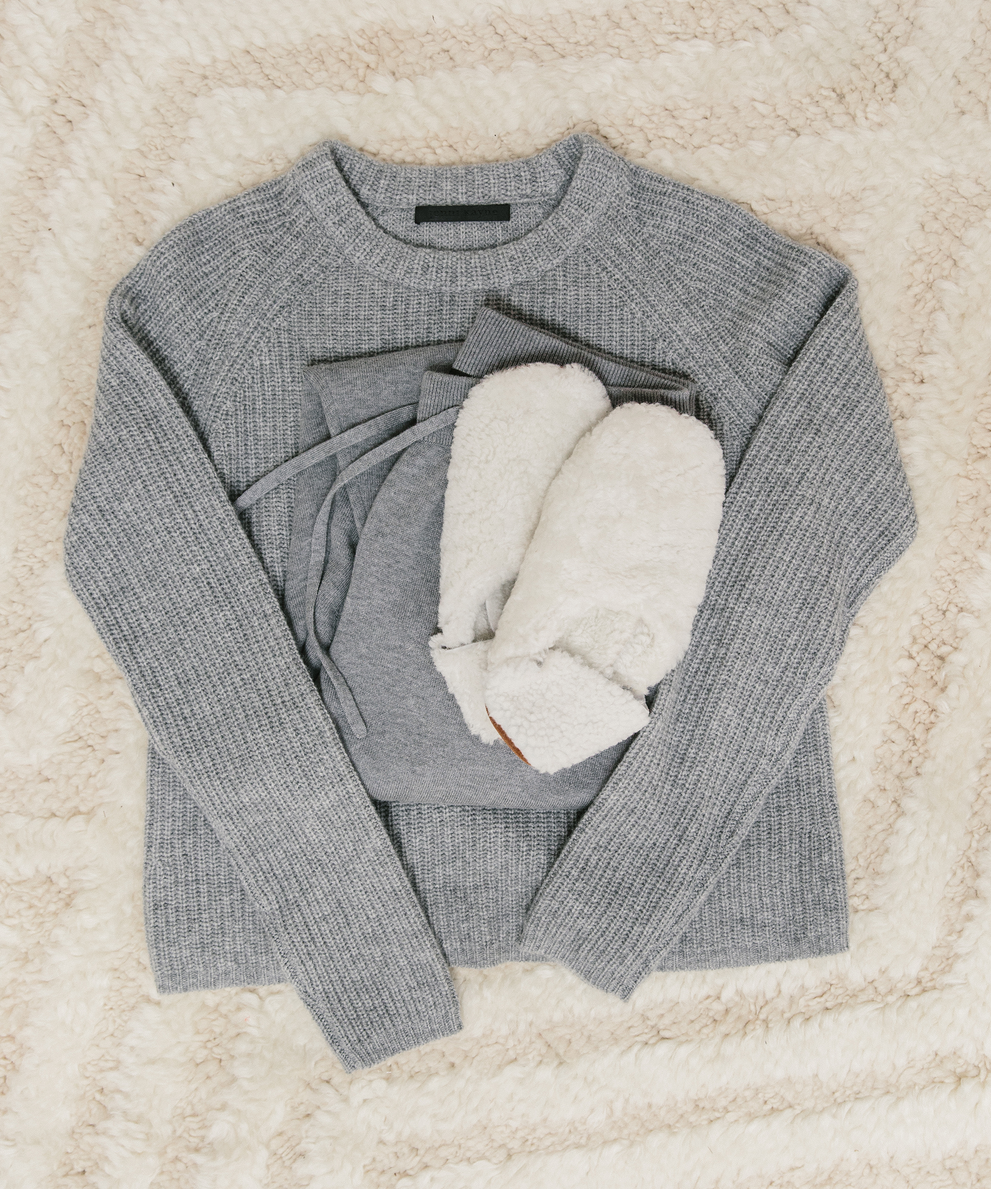 Grey Cashmere Fisherman Sweater and joggers with shearling slippers sitting on top of a textured rug.