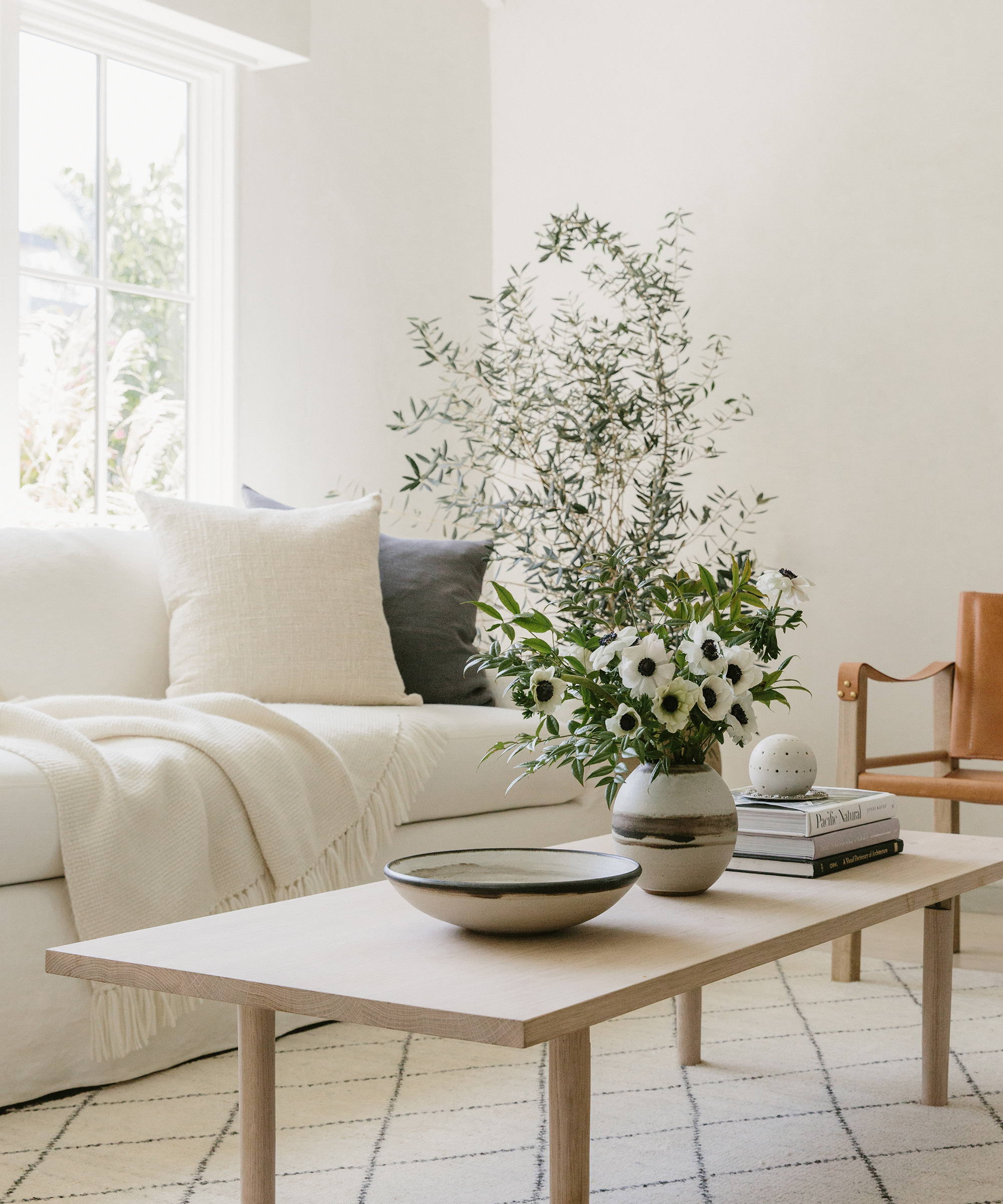Image of a living room with a focus on the canyon coffee table with ceramics and vases on top, and an ivory harbor sofa behind it with an assortment of pillows and throws.