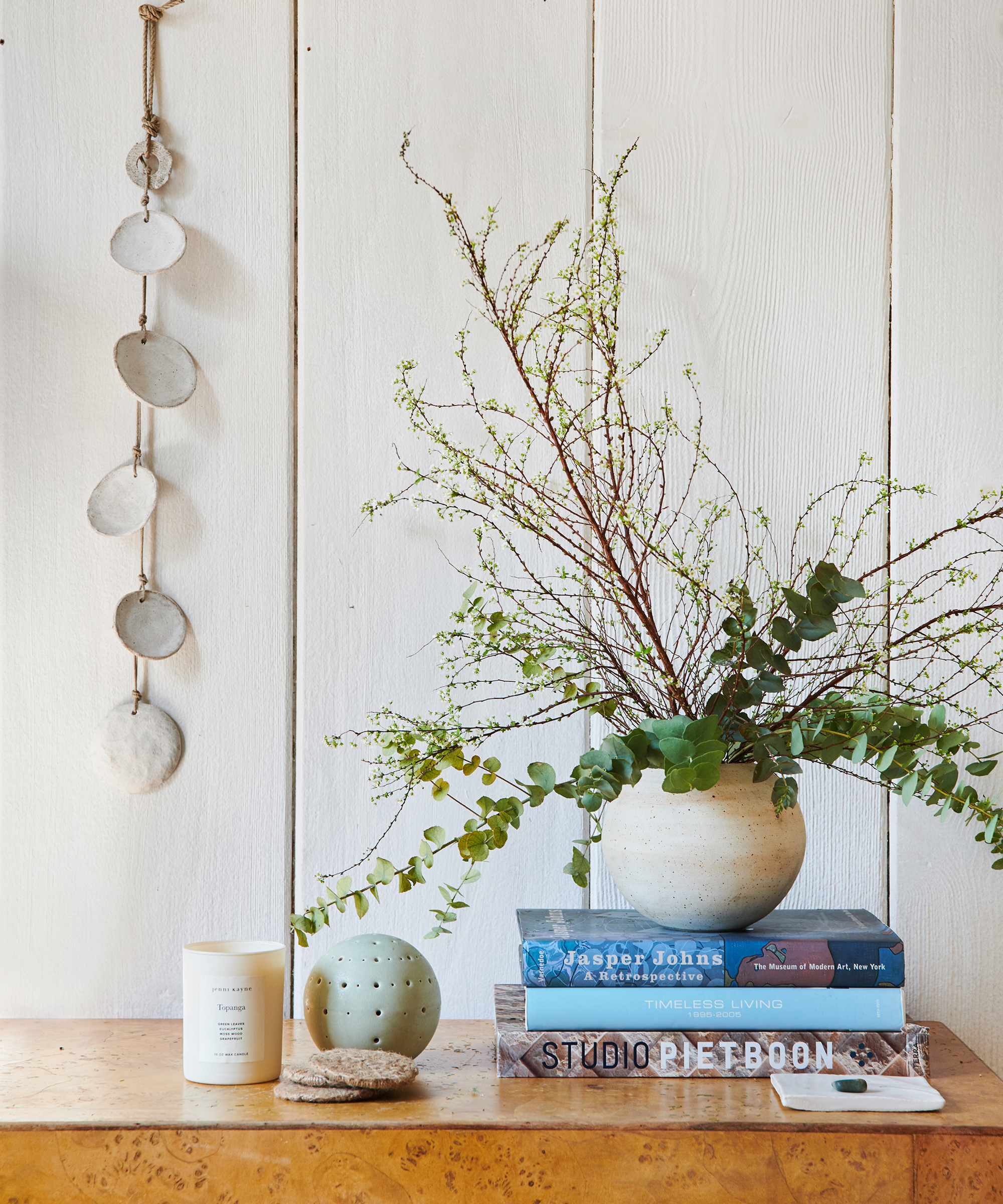 Close up shot of a ceramic strand hanging above an entryway table with books and greenery atop.