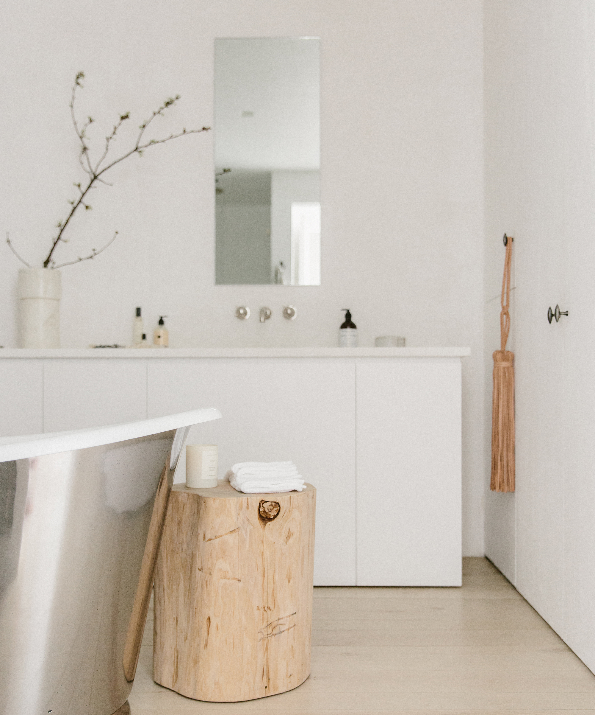 Bathroom shot with edge of a bathtub, cedar stump, and woven wall hanging on a doorknob.