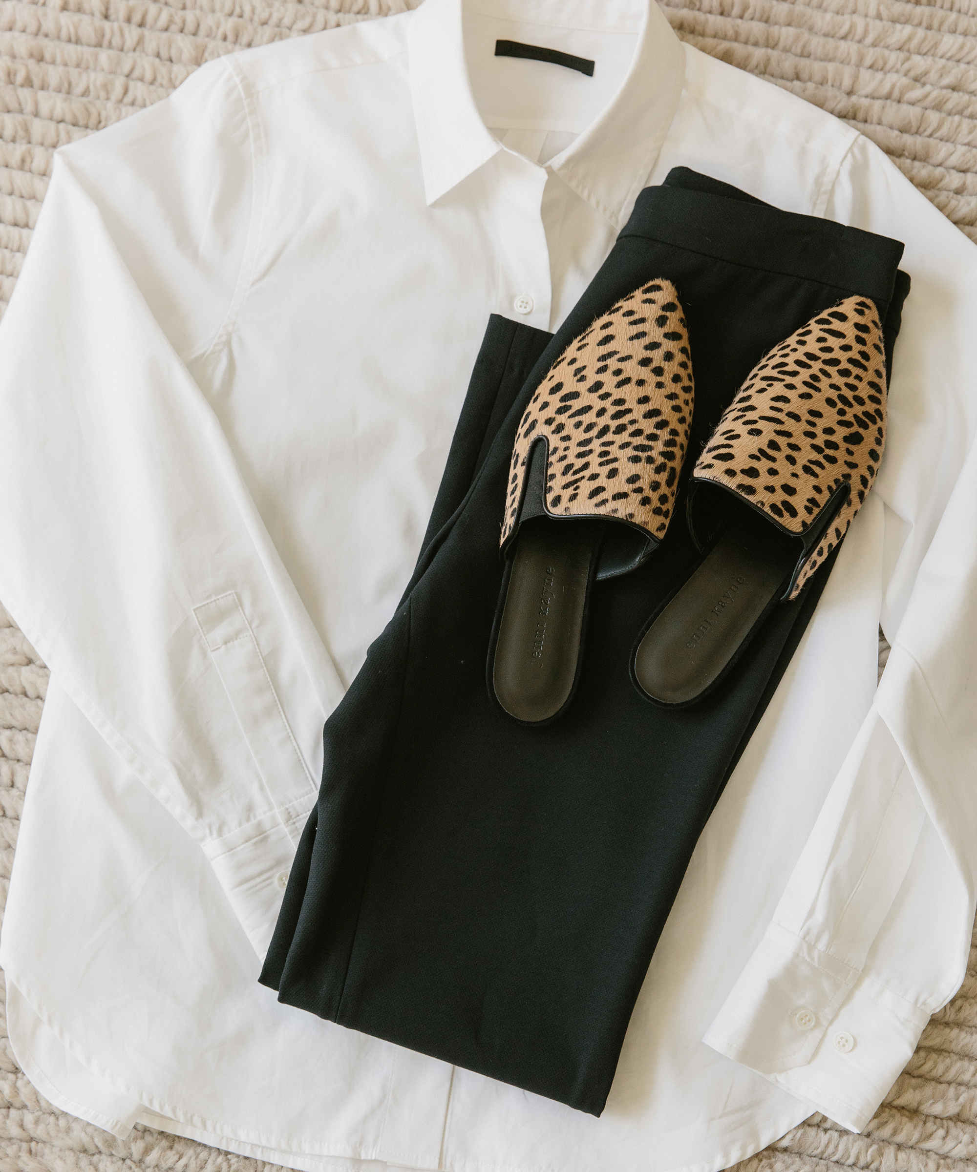 White button-up, black pants, and cheetah mules on a carpet.