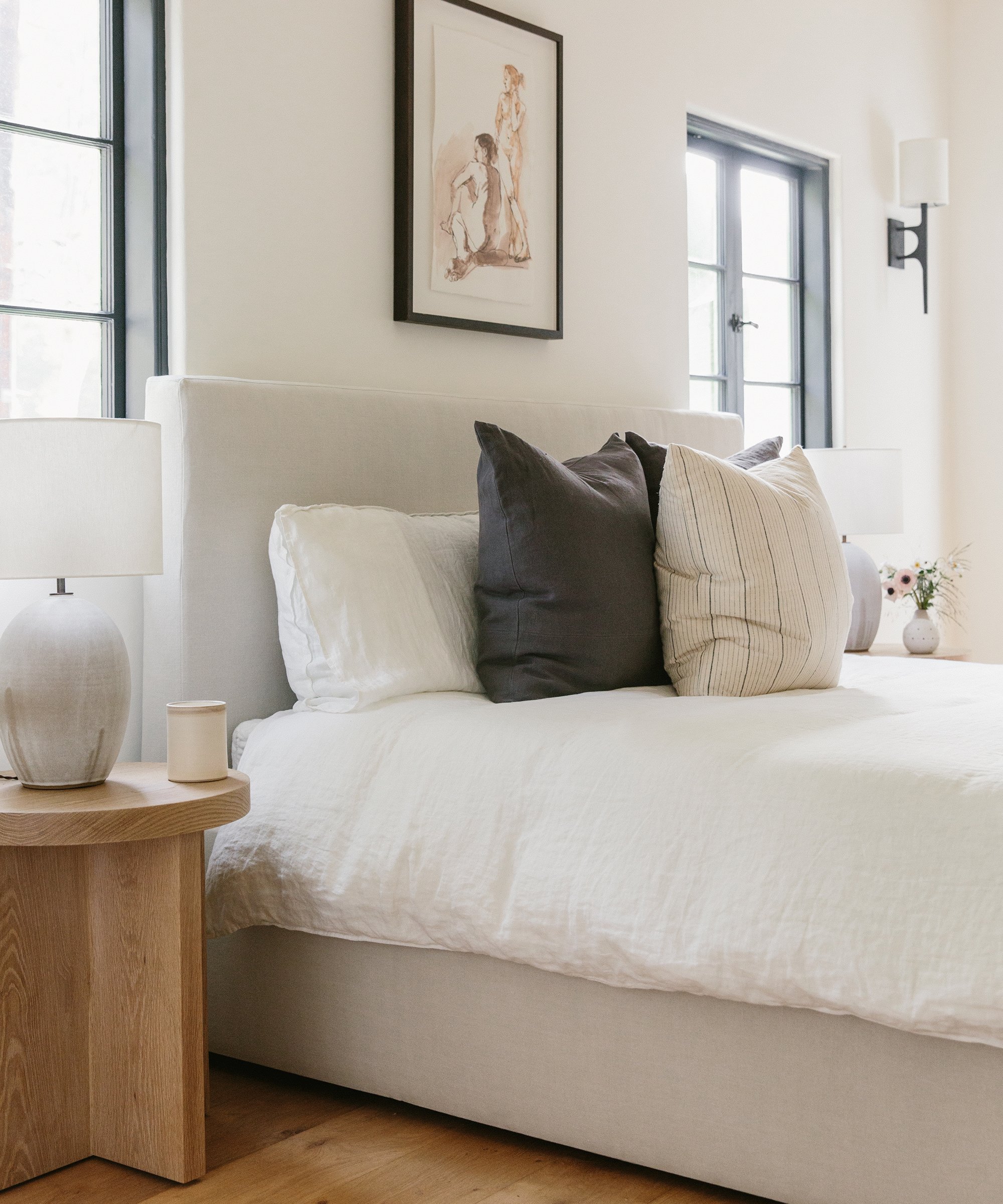 Side shot of a bedroom with Jenni Kayne pacific bed, oak side table, ceramic candle, and linen pillows.