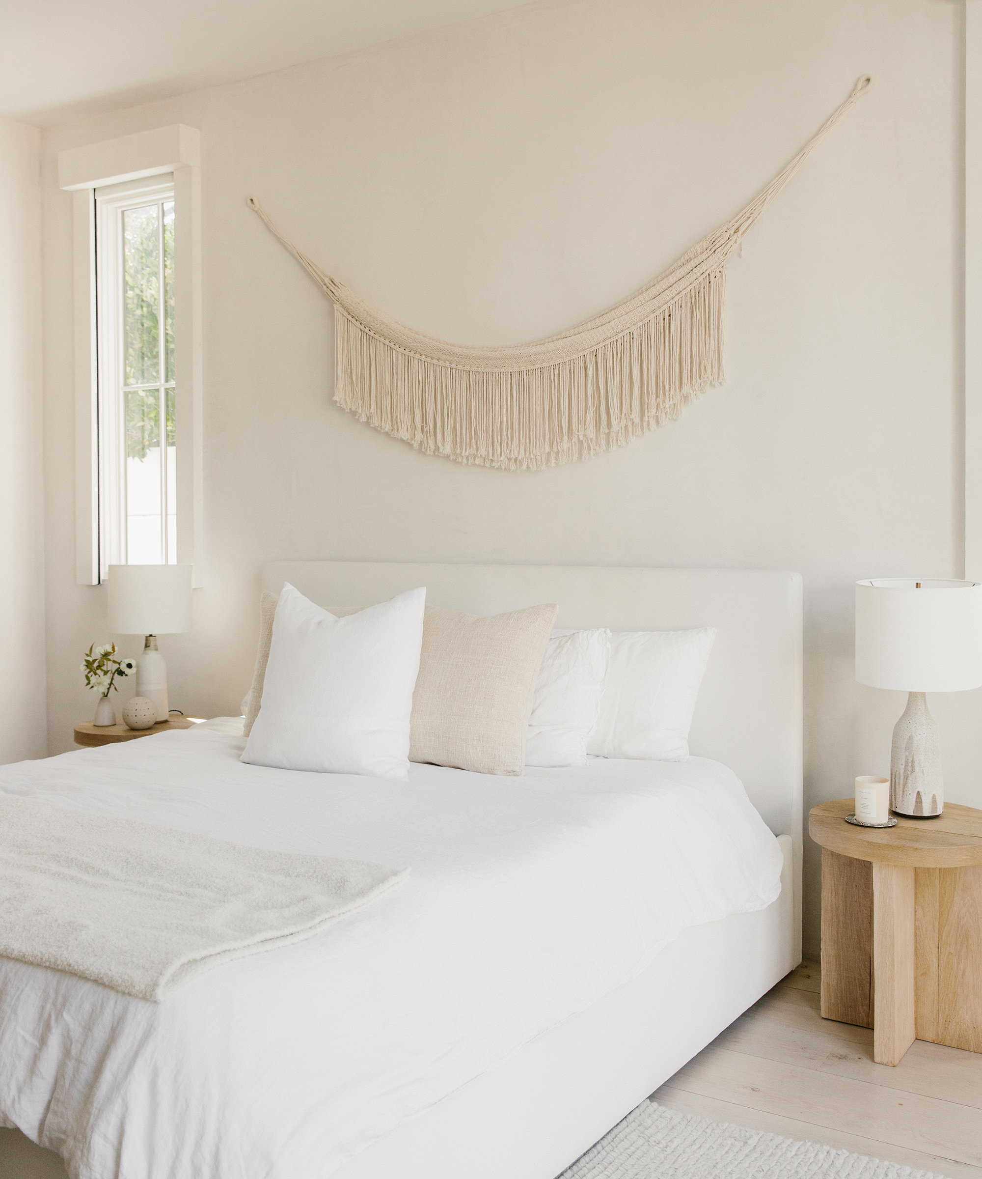 Bedroom with Jenni Kayne pacific bed, white and ivory linens, woven wall hanging above, and two oak side tables.