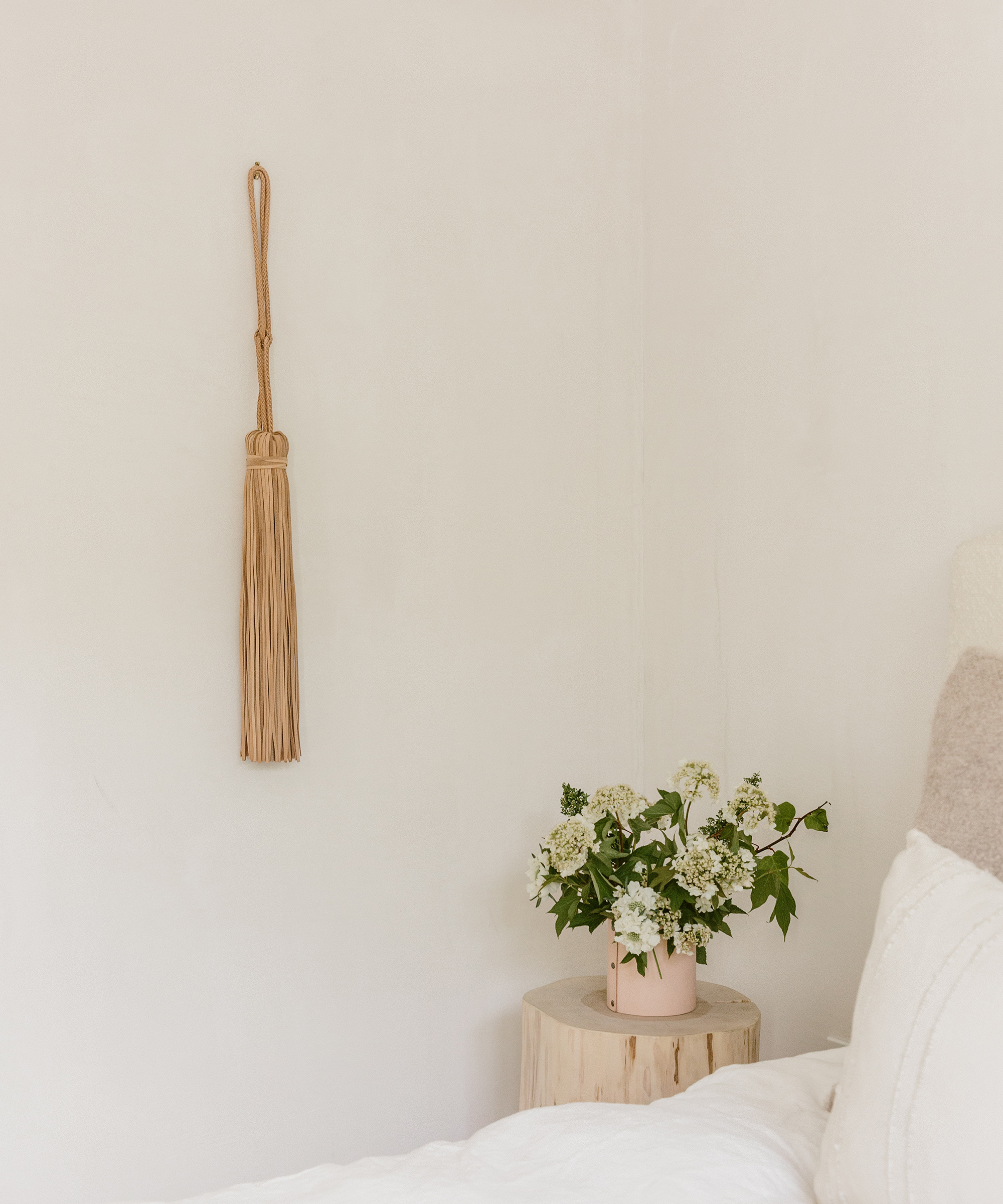 Bedroom wall with Jenni Kayne leather wall hanging and cedar stump with leather rivet vase with flowers inside.