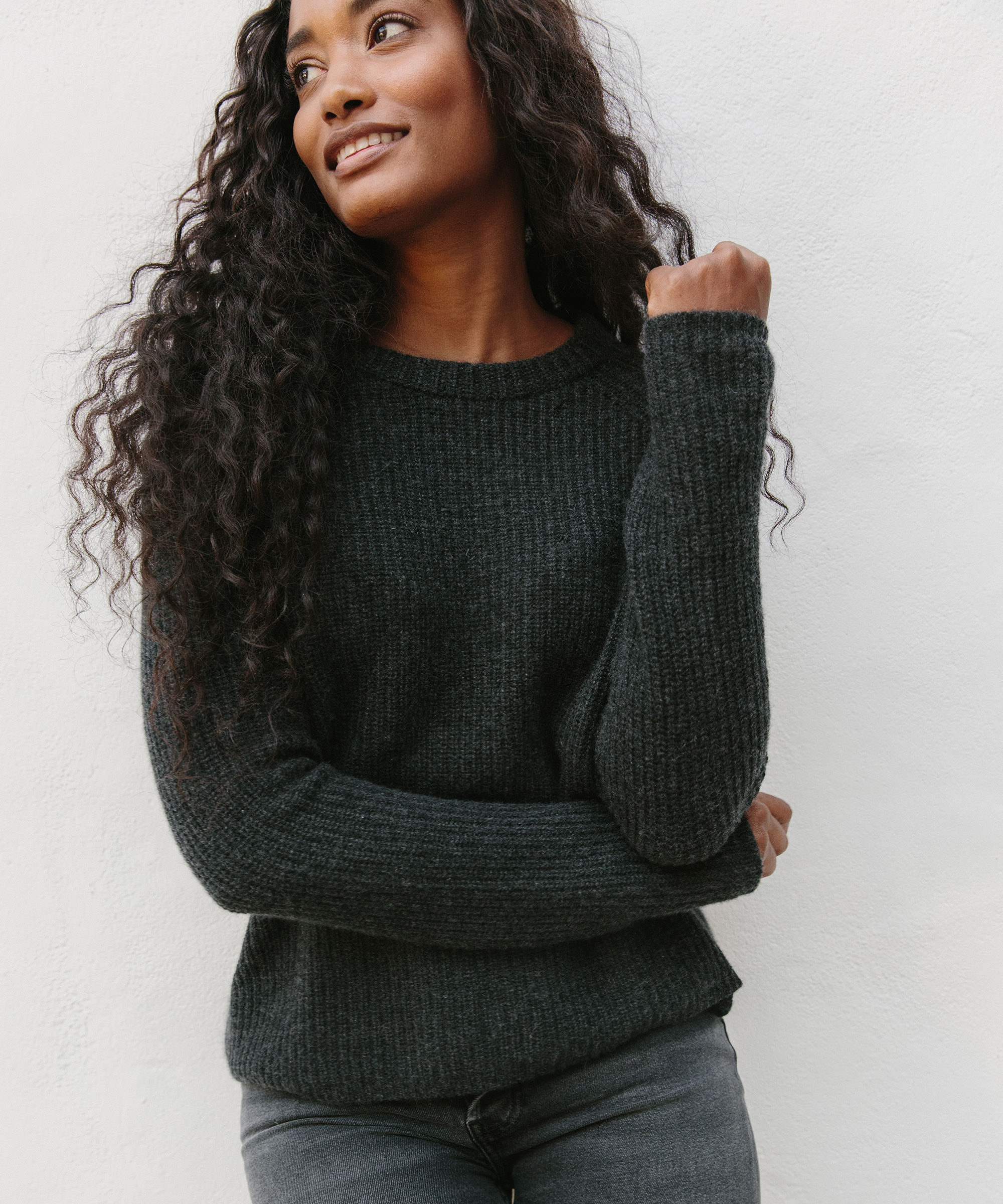 Jenni Kayne model wearing cashmere fisherman sweater in charcoal and black pants standing in front of a white wall.
