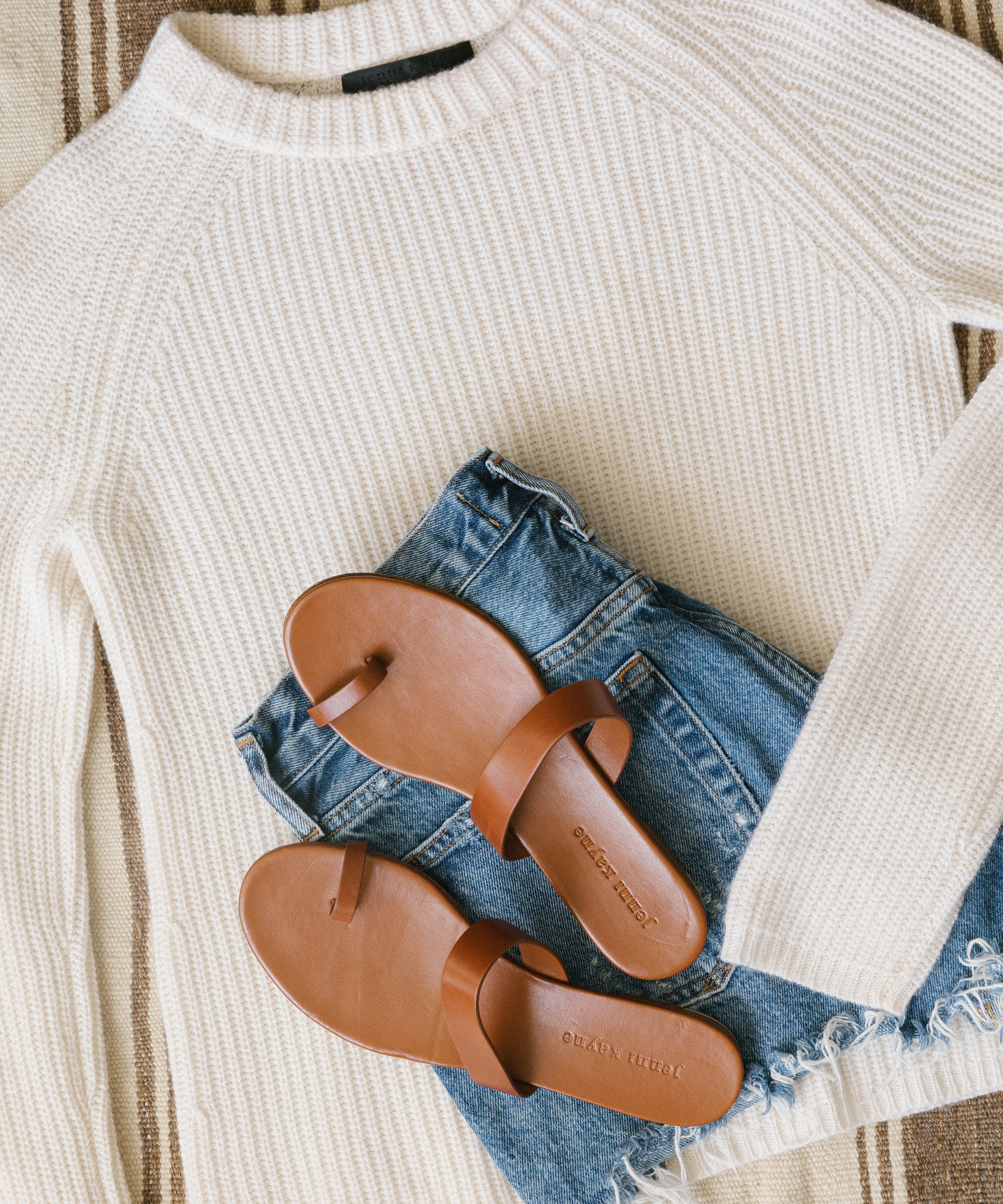 Jenni Kayne ivory cotton fisherman sweater with leather strap sandals and denim shorts.