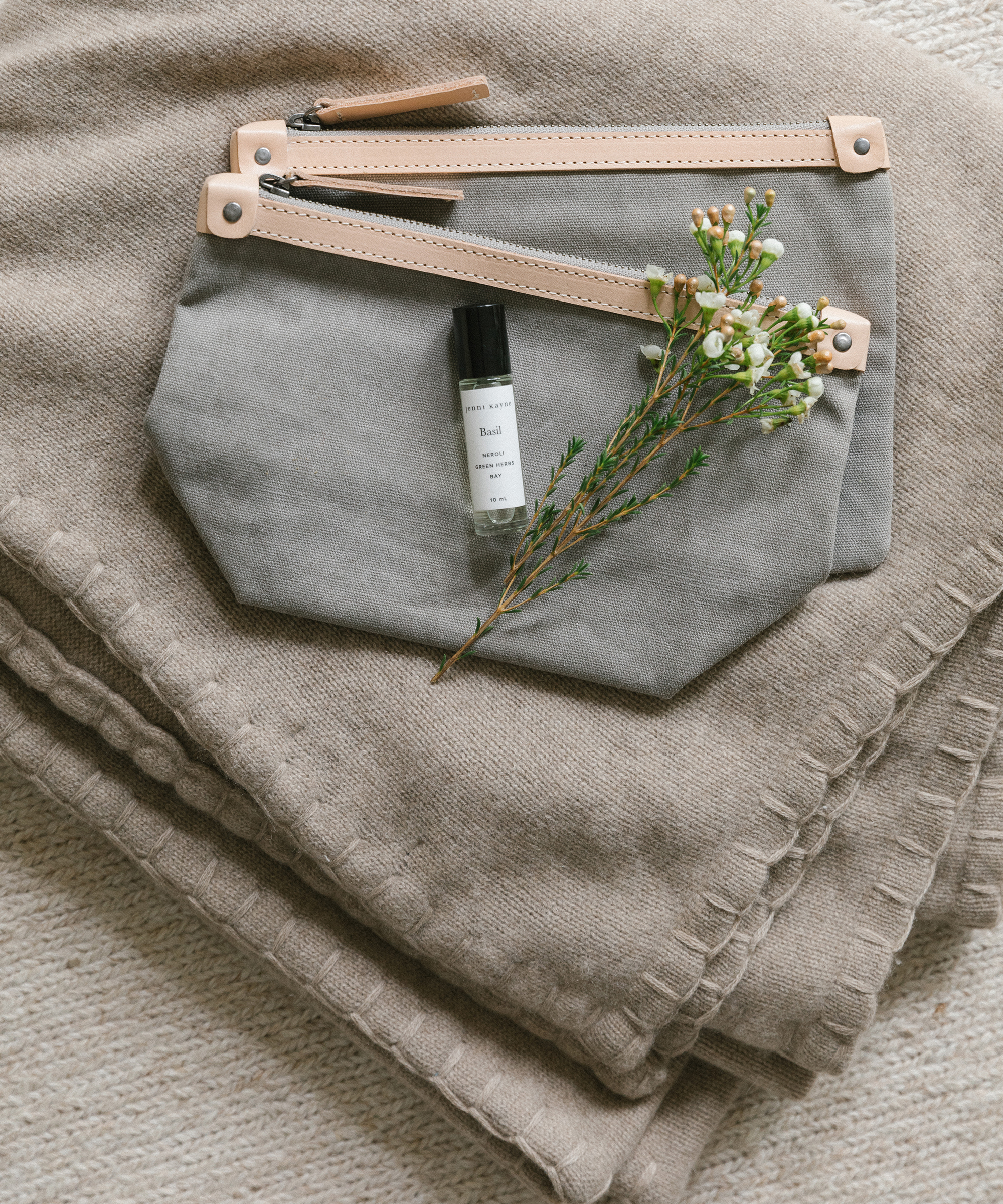 Jenni Kayne tahoe cashmere throw in taupe with cotton travel pouches and roll-on oil on top.
