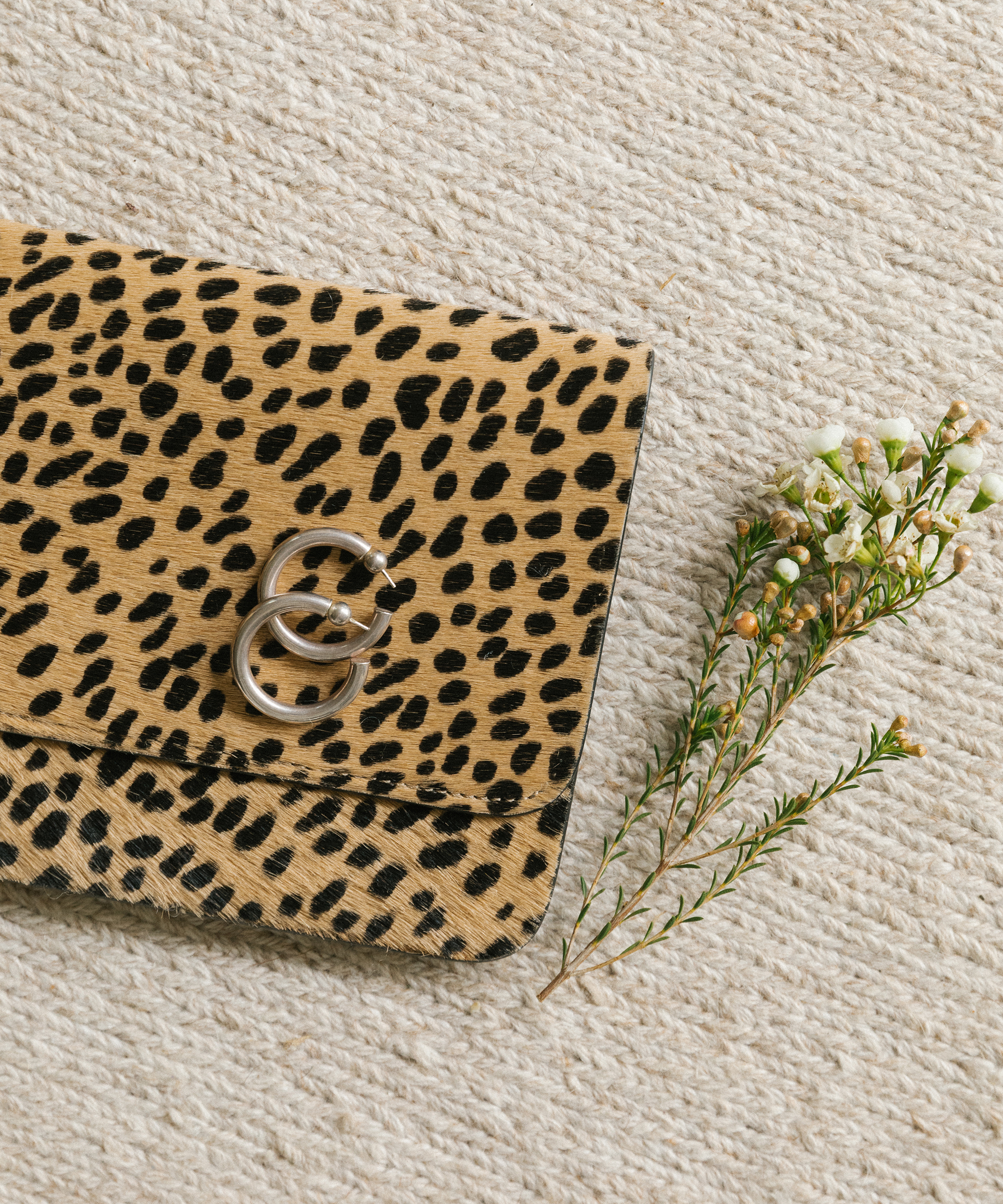 Jenni kayne cheetah clutch with everyday hoop earrings and florals on a carpet.