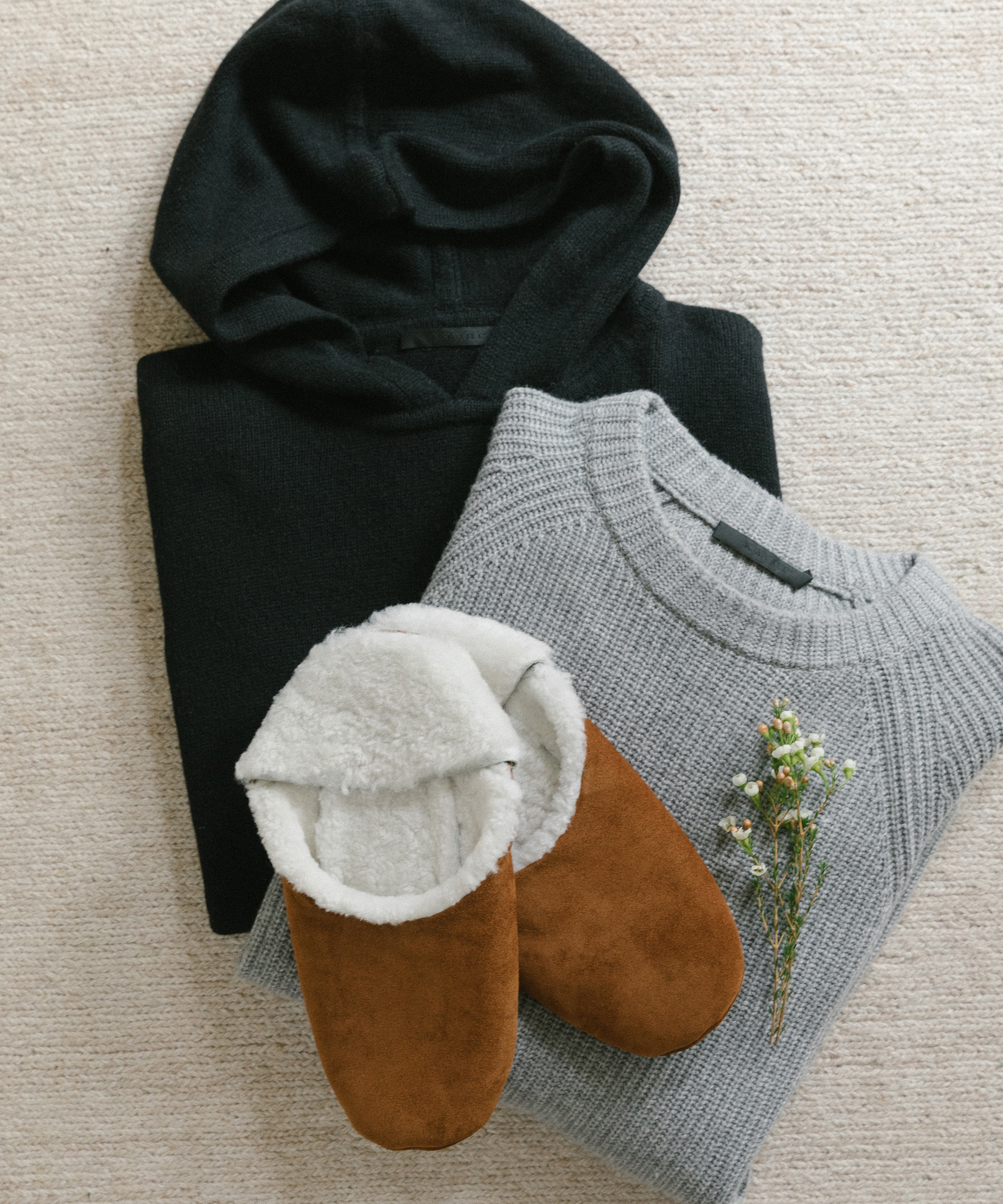 Jenni kayne men's fisherman hoodie and sweater folded up next to shearling slippers in saddle.