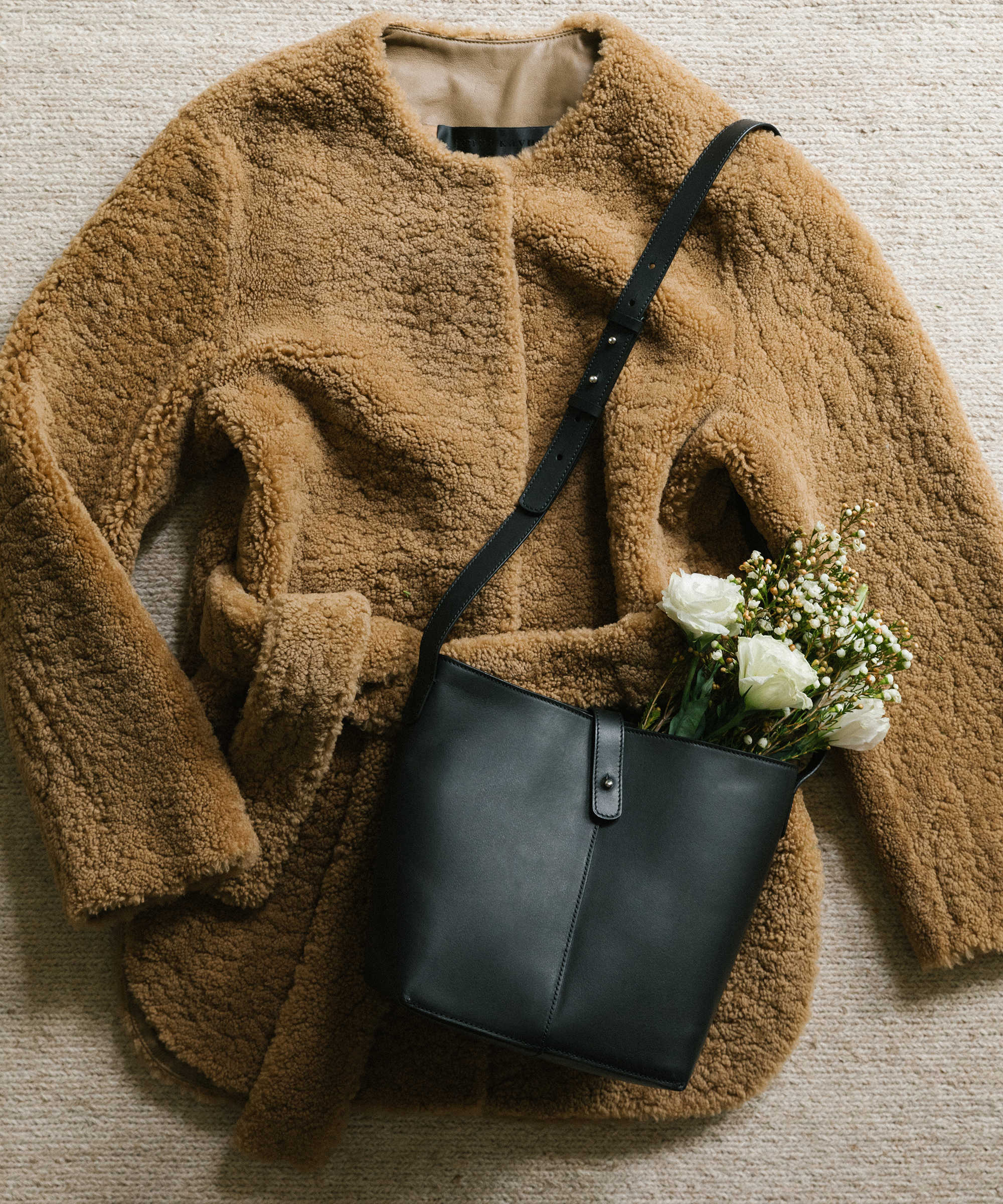 Jenni Kayne shearling yves jacket and mini leather bucket bag on the ground with flowers.