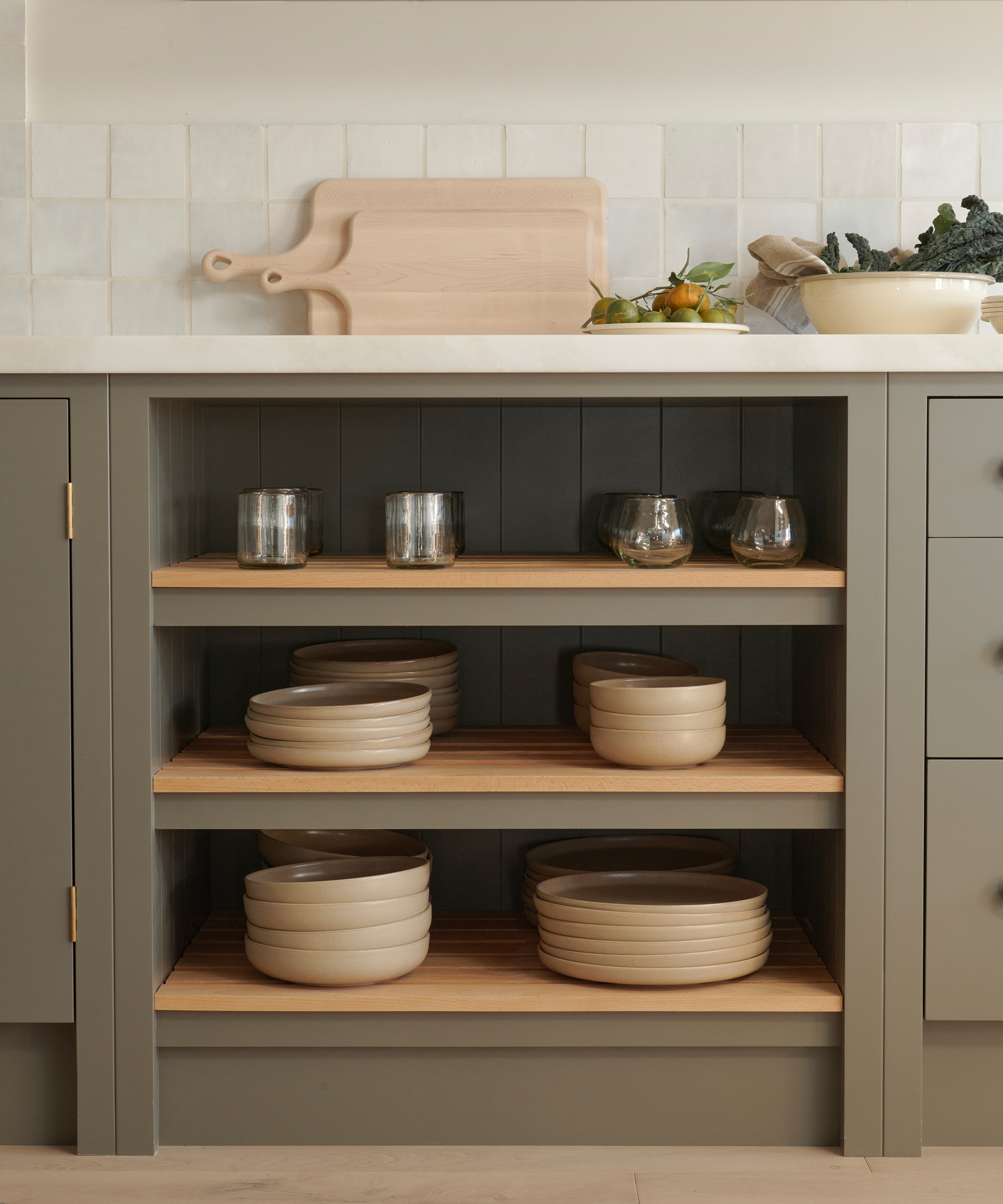 lower green kitchen cabinets with open shelving holding dinnerware items and glasses