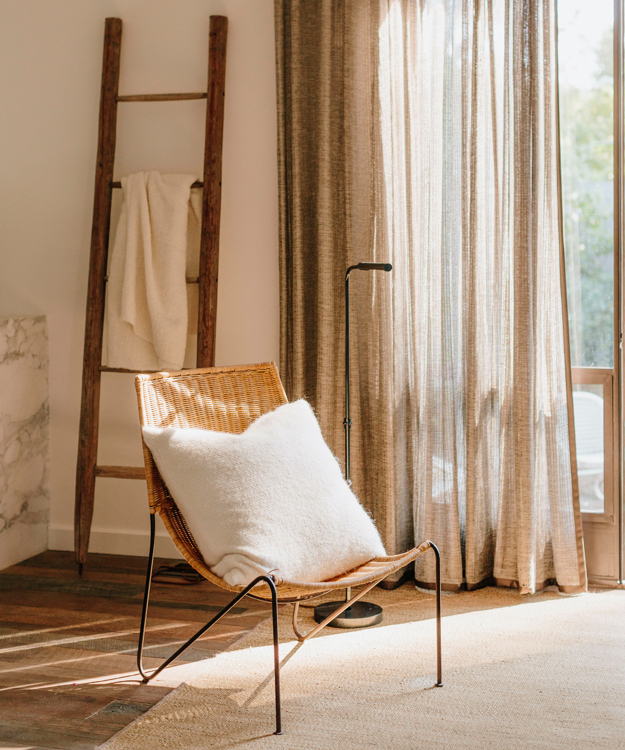 Brit Hines' montecito guest room with a wicker chair and alpaca basketweave pillow in ivory on top with a ladder in the background.