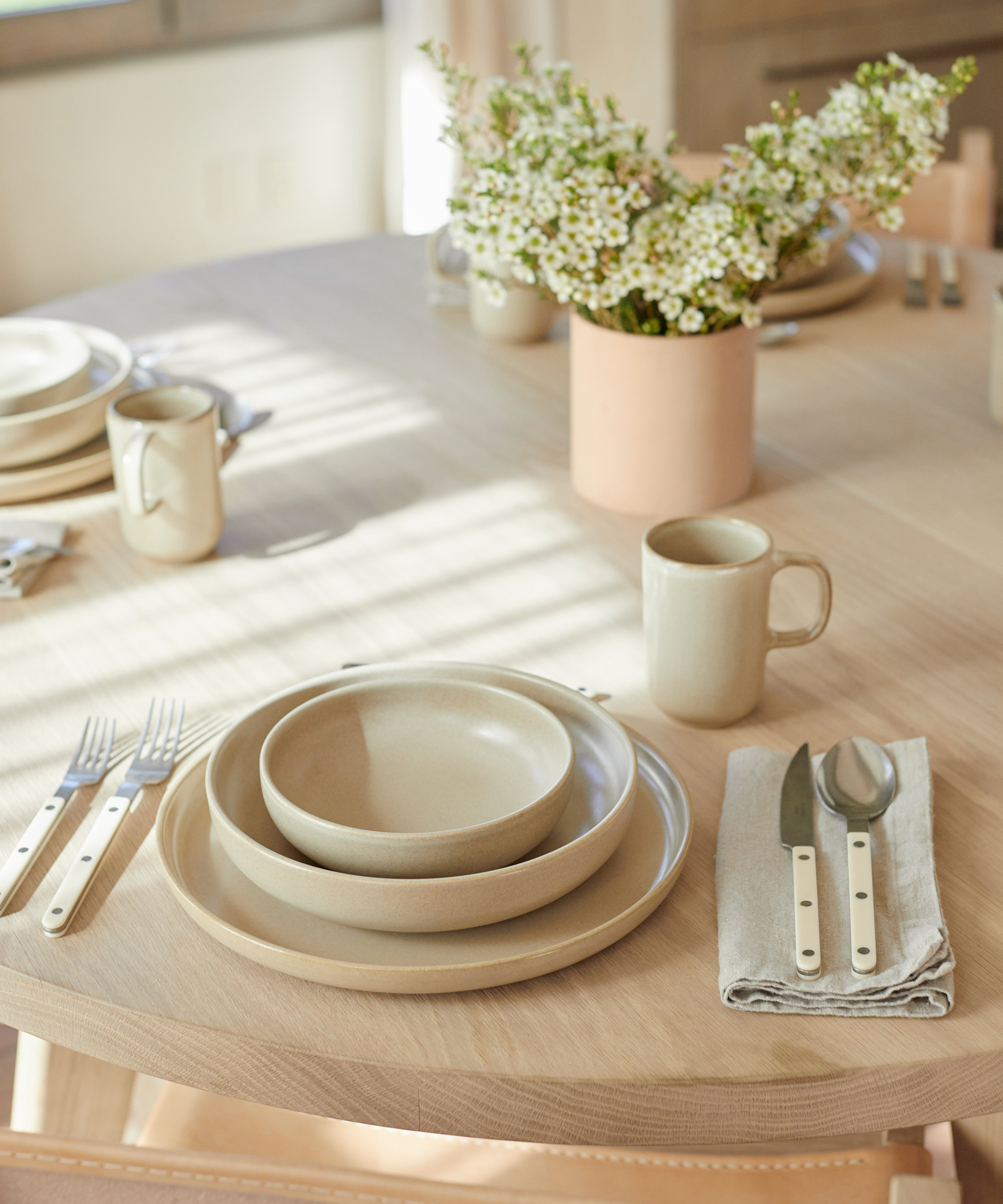 Pacific Dinnerware set sitting on the jenni kayne round dining table with bistro cutlery and frayed linen napkins.