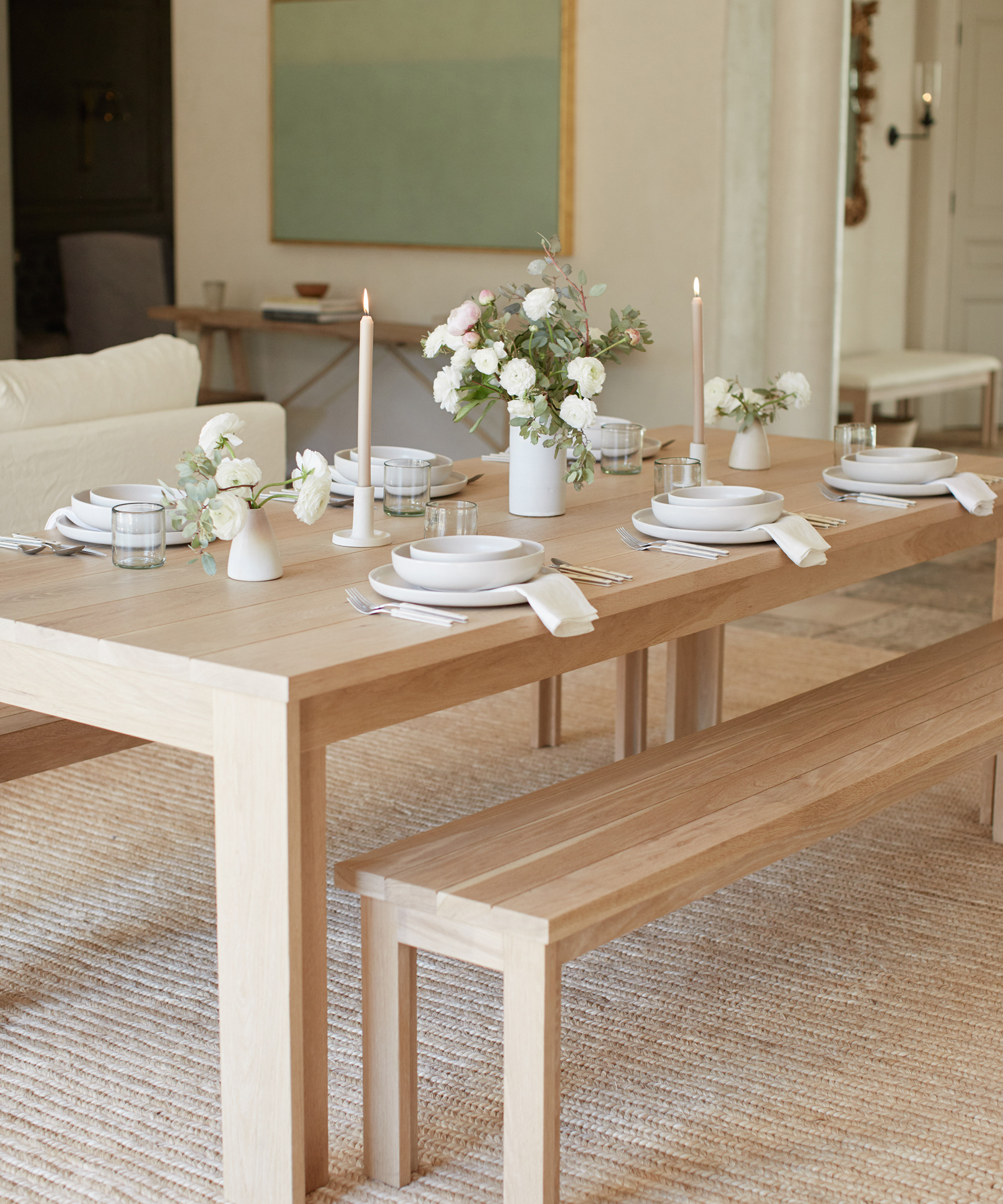 Jenni Kayne dining table in the dining room with dining bench set with pacific dinnerware and vases of flowers.