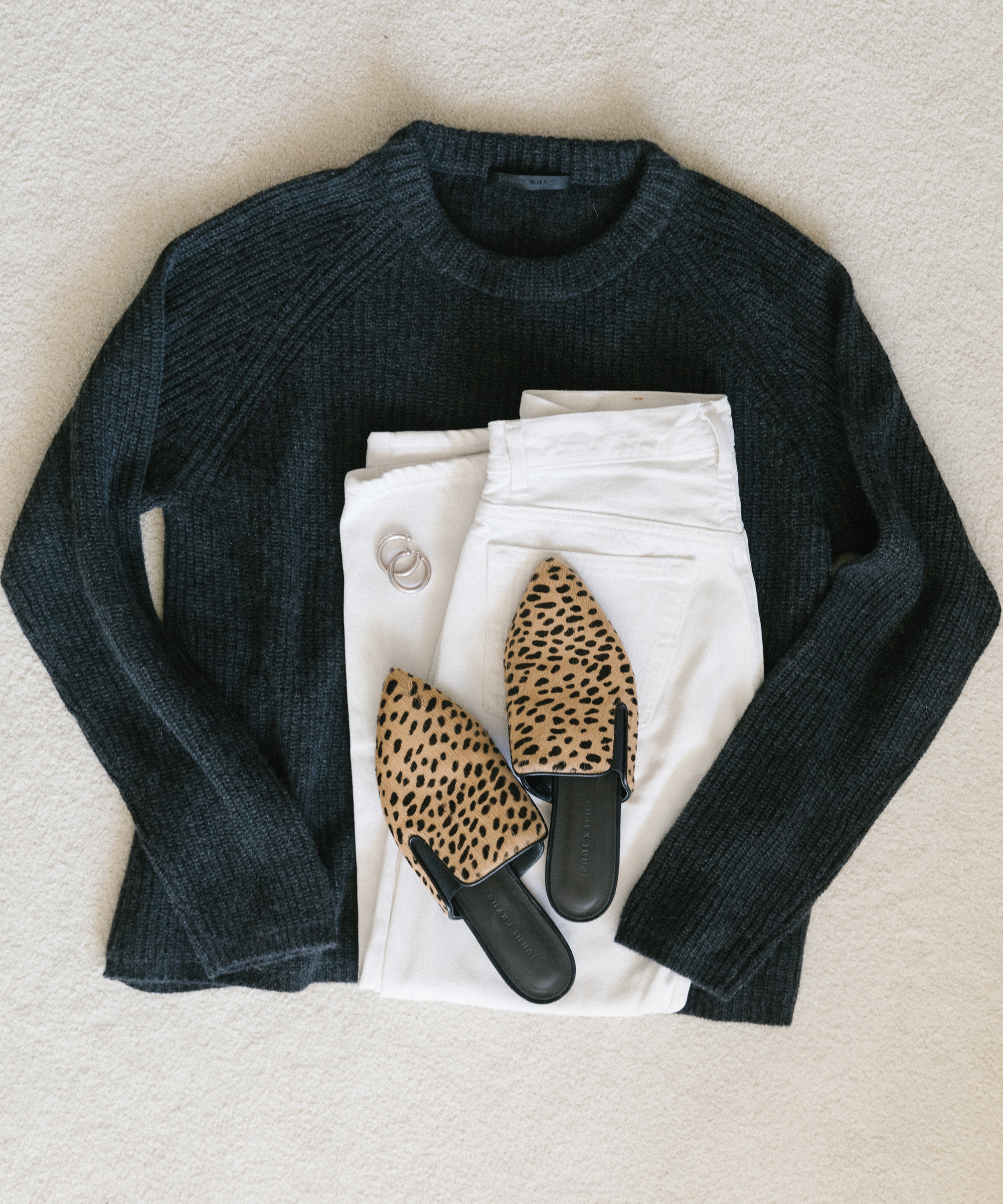 Laydown of jenni kayne cashmere fisherman sweater in charcoal with white pants, hoop earrings, and cheetah mules on white carpet.
