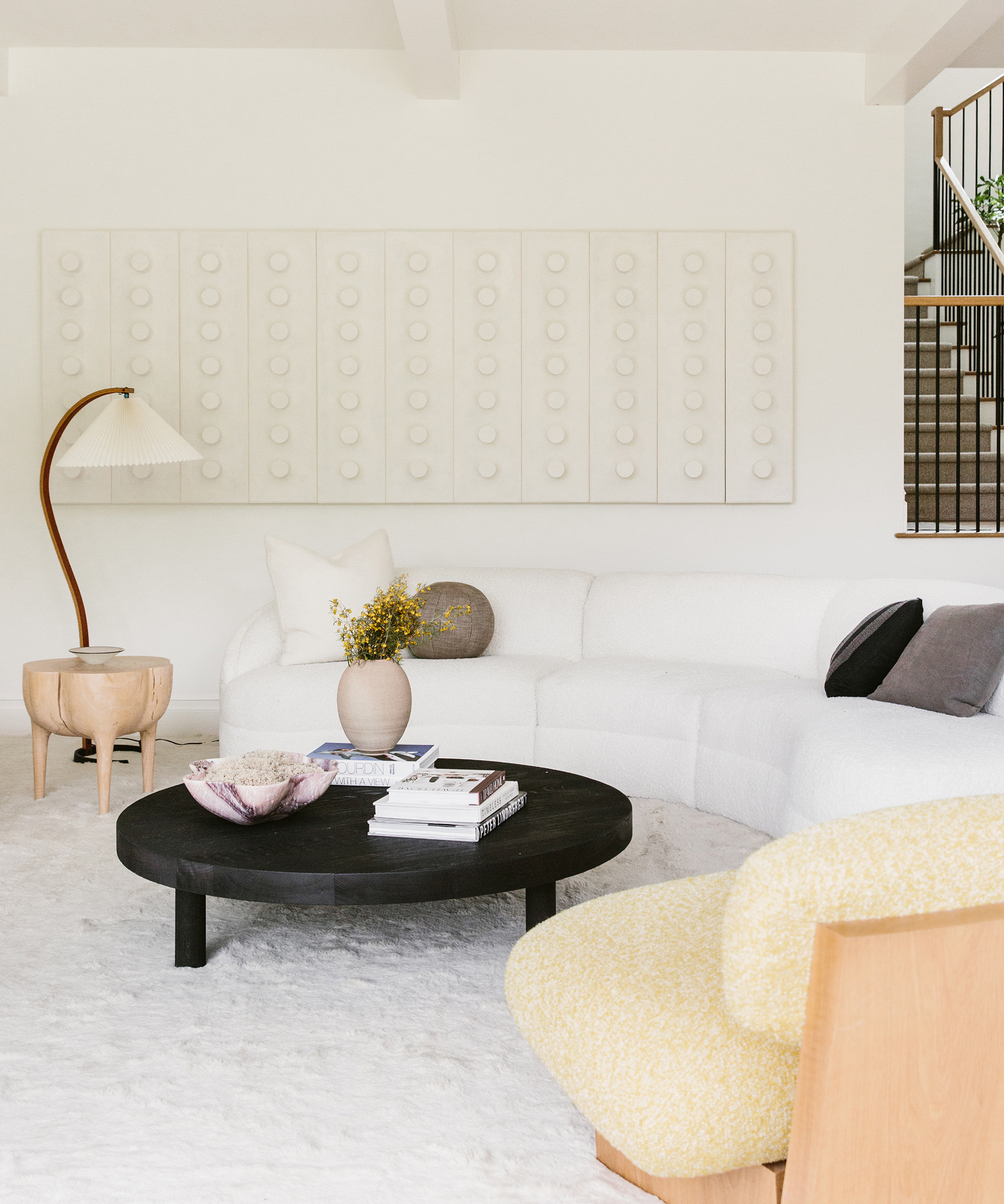 Transition State designed living room with white rug, black coffee table, accent light fixture, boucle sofa, and long piece of art hanging above the sofa.
