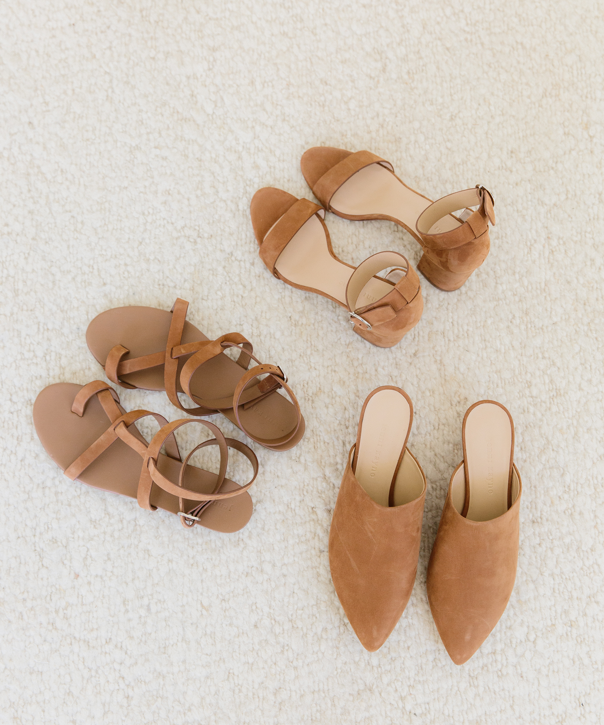 Three pairs of tan women’s shoes—strappy flat sandals, low-heeled ankle-strap sandals, and pointed-toe mules in soft spring colors—are arranged on a light textured carpet.