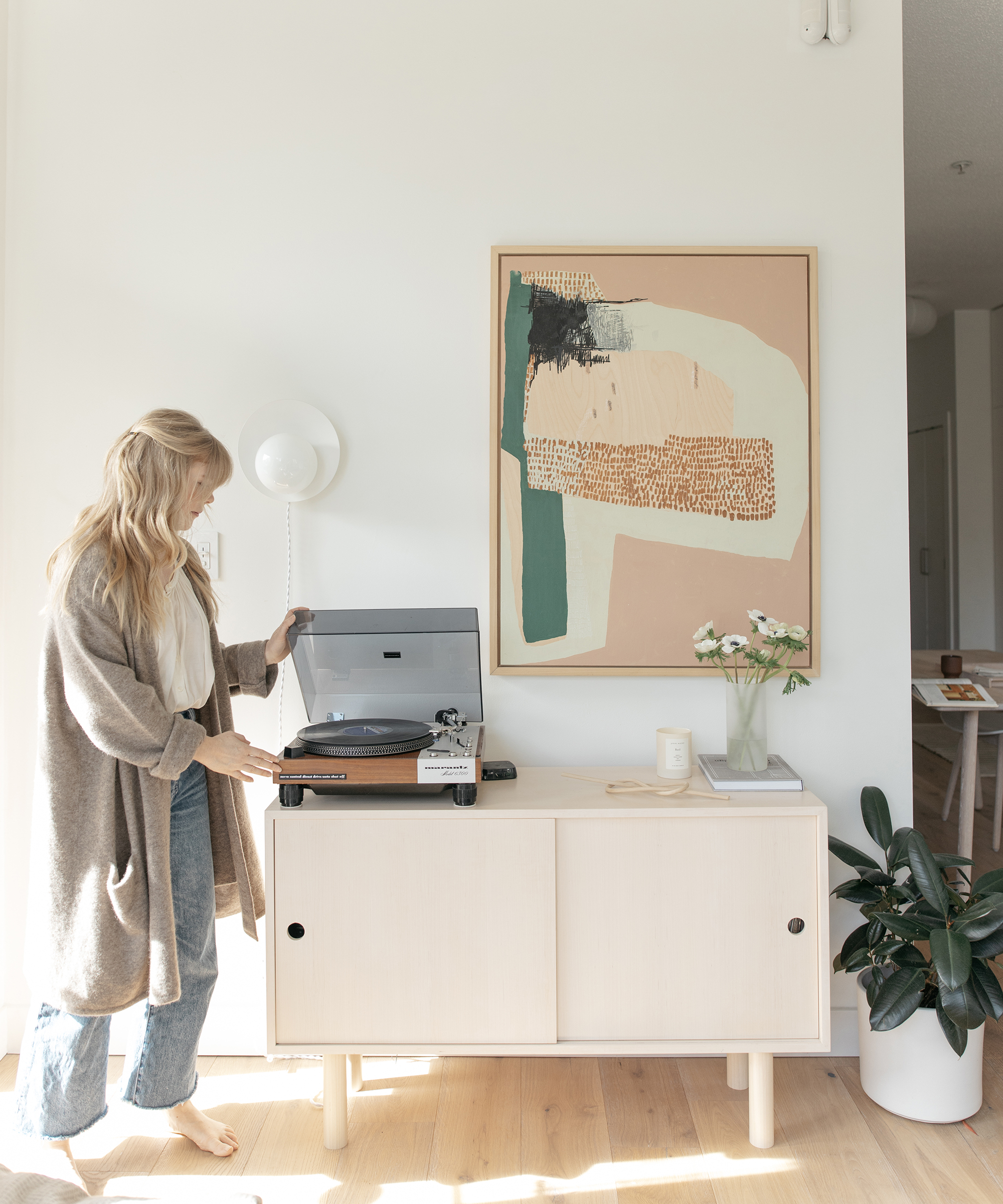 Alison Mazurek of 600sqftandababy in her living room opening a record player wearing a jenni kayne sweater coat.
