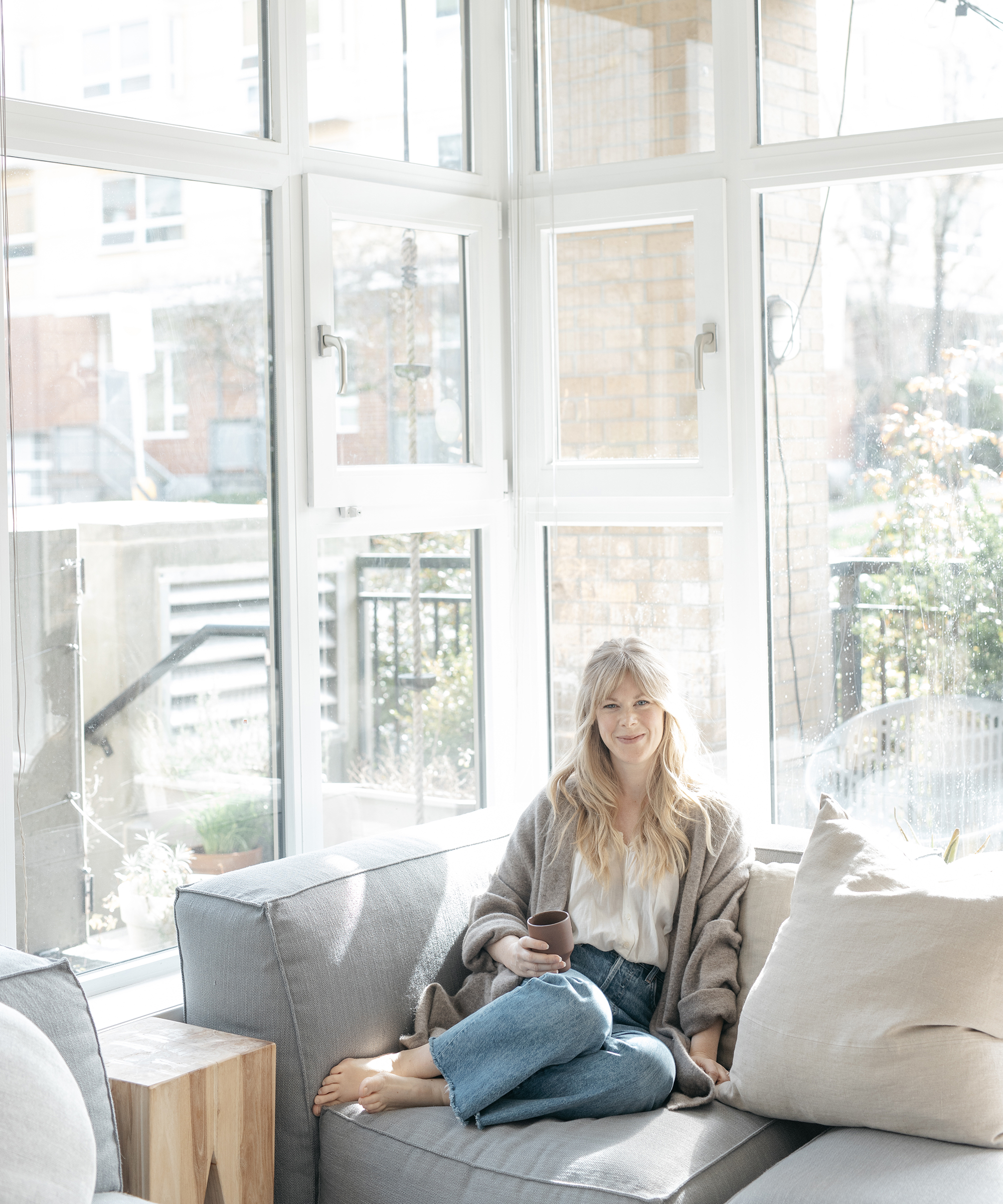 Alison Mazurek sitting on the sofa in her Vancouver apartment wearing jenni kayne sweater coat.