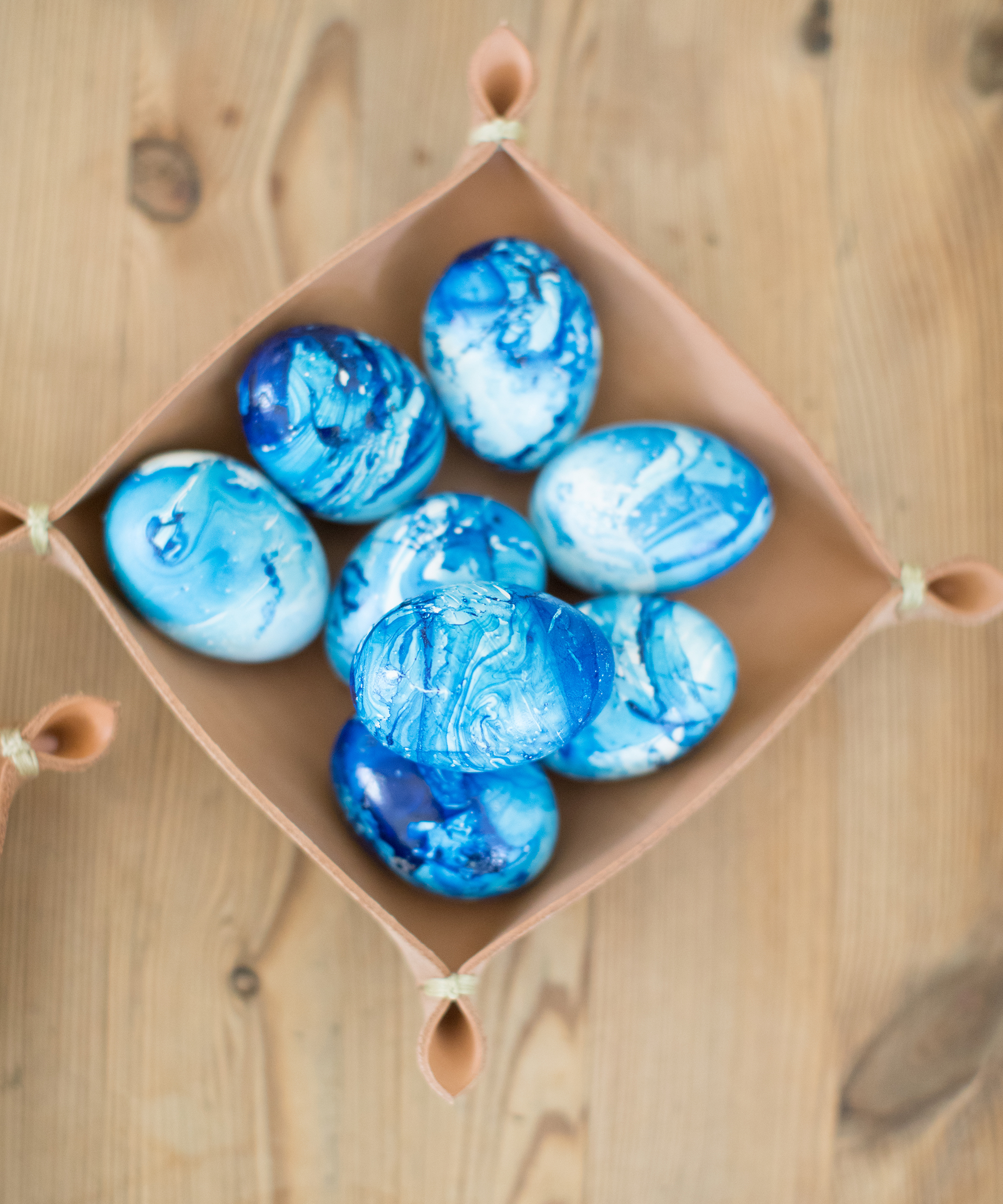A square tan container holds ten blue and white marbled Easter eggs, viewed from above, on a light wooden surface—perfect inspiration for Easter crafts.