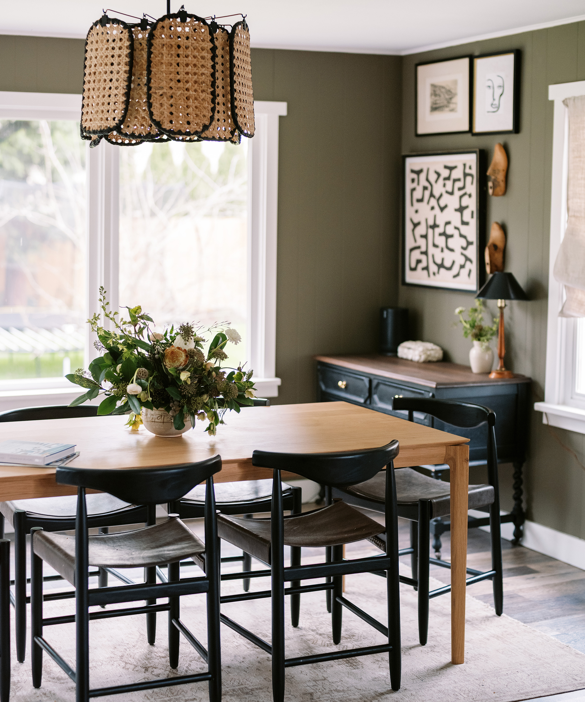 Kennesha Poe-Buycks of Restoration House's dining room with wooden table, black chairs, rustic light fixture, and a flower arrangement on the table.
