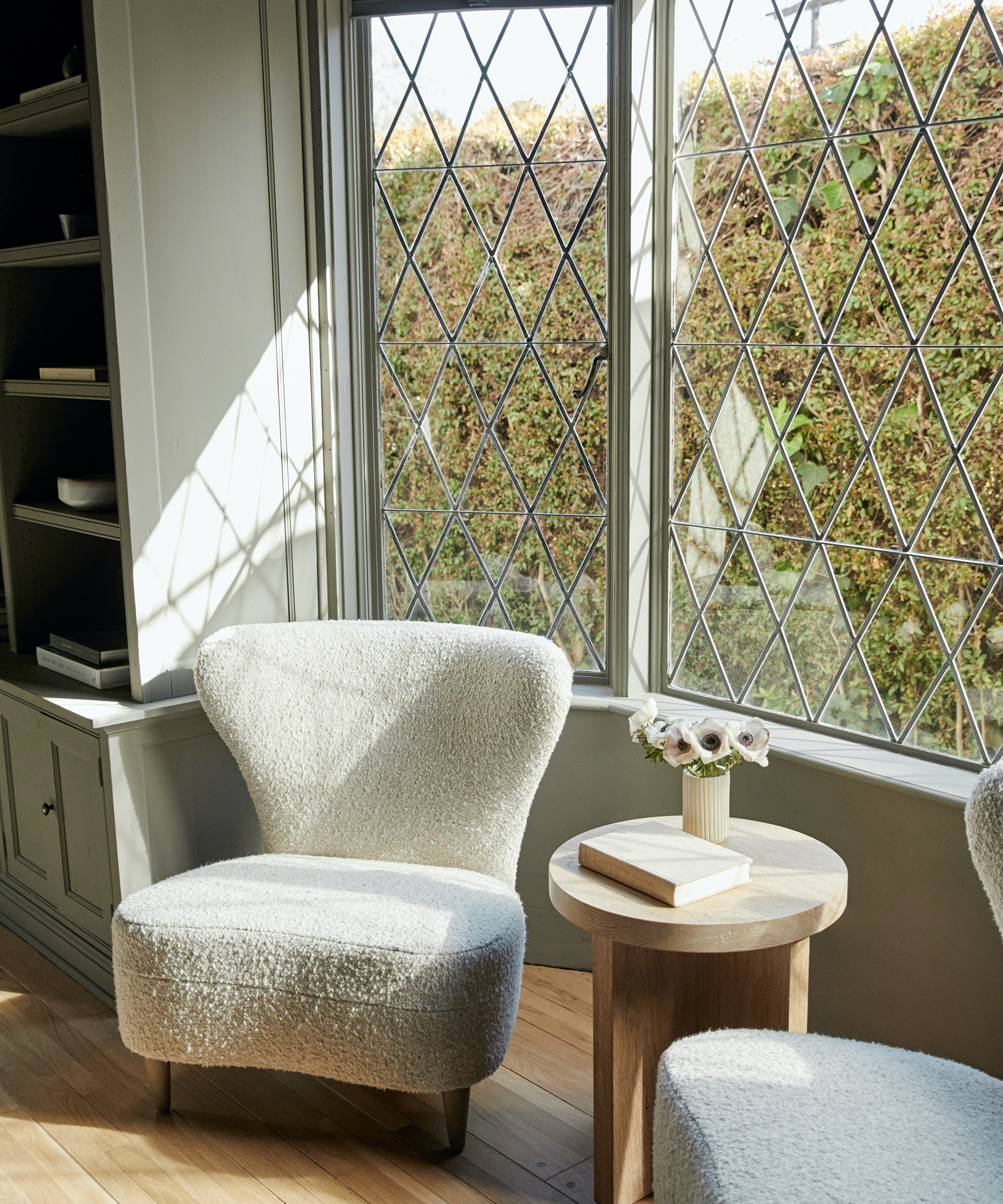 Jenni Kayne shot of a den with a brentwood boucle chair sitting by the window in the sunshine with an oak side table next to it.