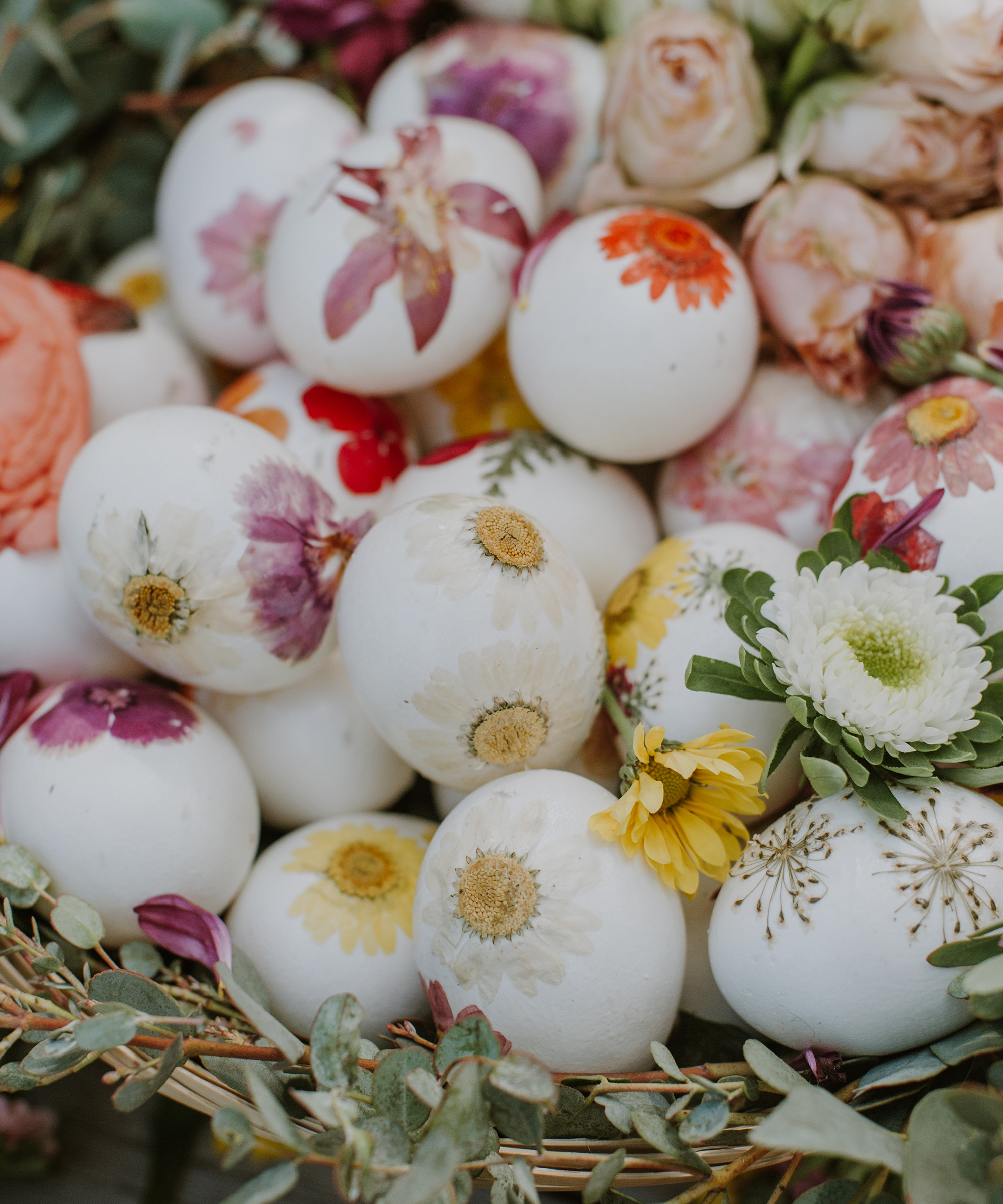 A basket of easter eggs with colorful flowers pressed onto them in a pile.