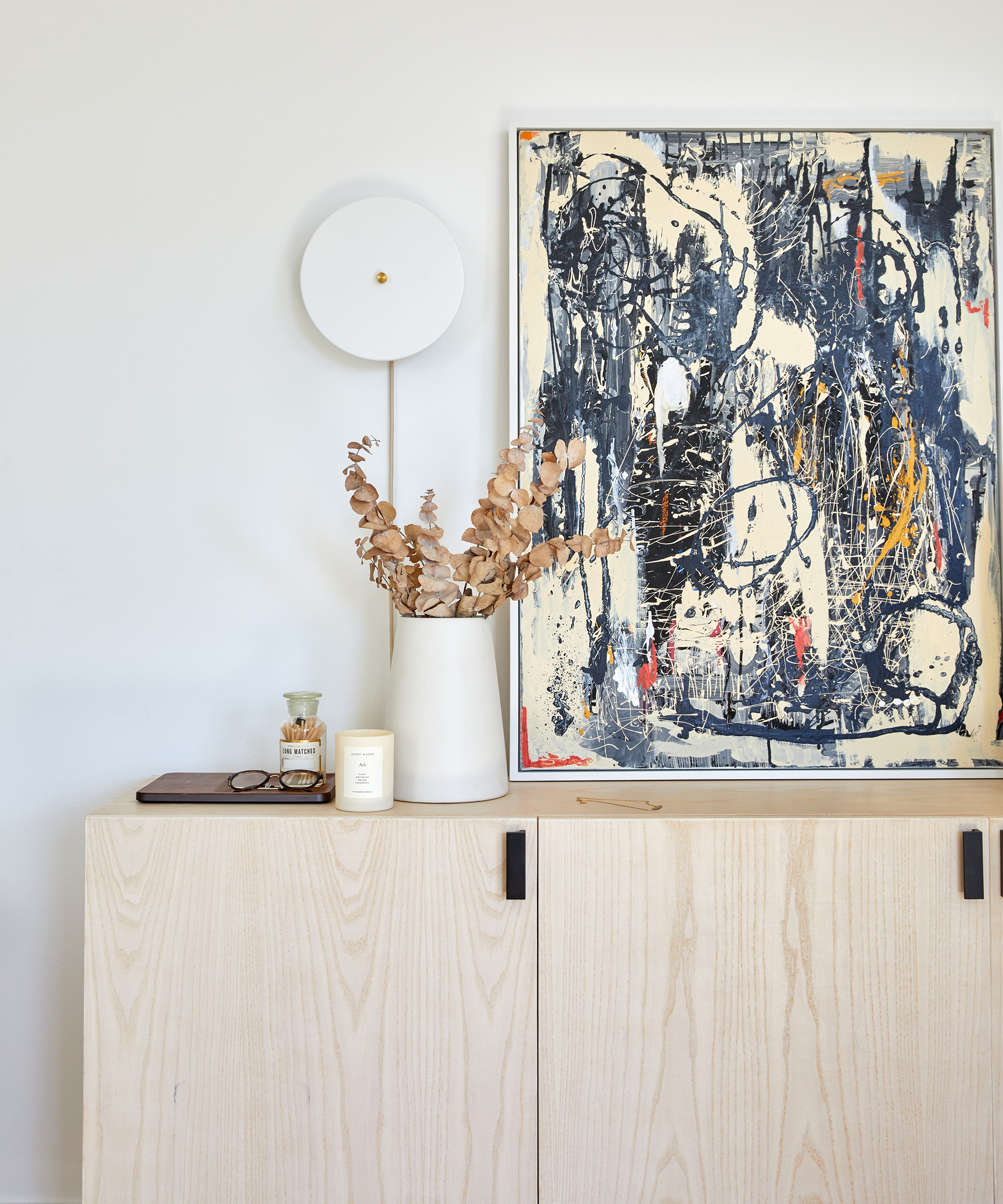 Interior designer Dani Arps' hallway with a white credenza and an assortment of pieces on top including a piece of art, a jenni kayne candle, and a vase with rustic flowers in it.