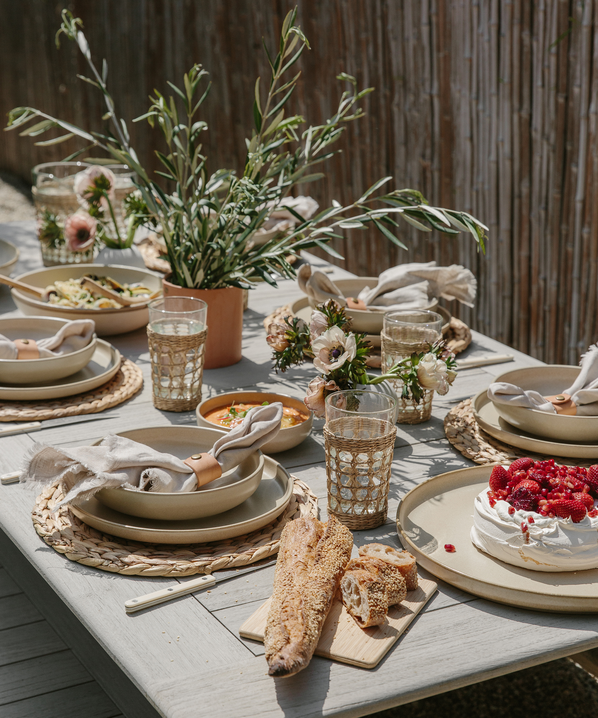 An outdoor tabletop with jenni kayne pacific dinnerware, leather rivet vase, woven chargers, and a spring menu.