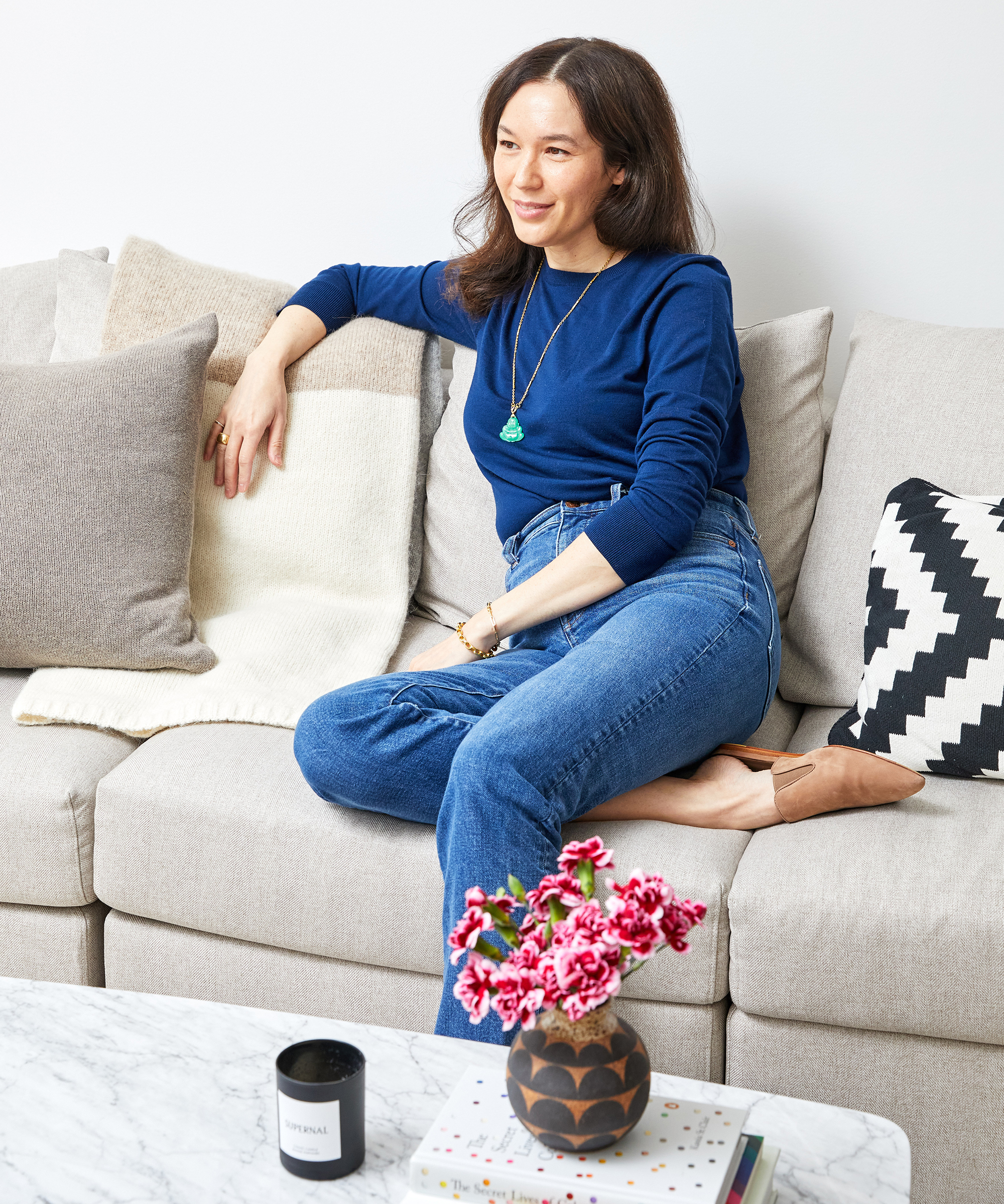 Melissa Medvedich sitting on her living room sofa wearing jenni kayne suede mules and crosby crewneck in navy.