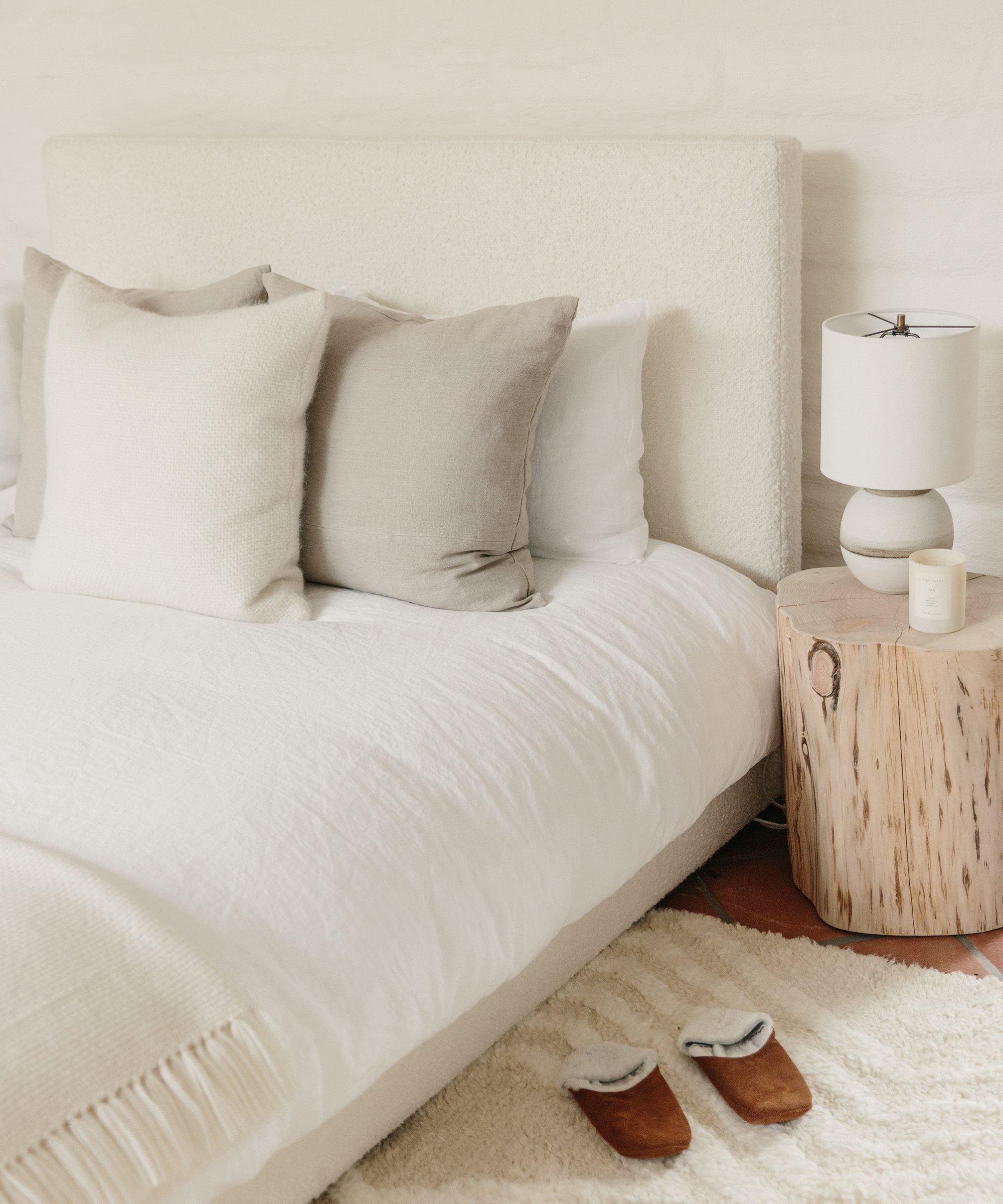 Jenni kayne pacific bed in ivory wool boucle with pillows on top, a cedar stump next to the bed, and slippers next to the bed.